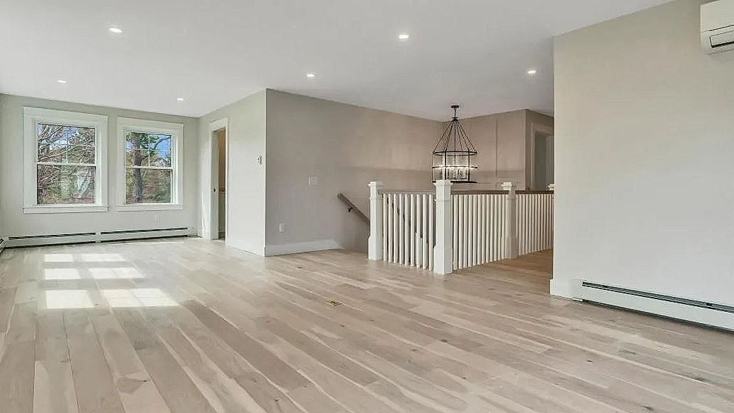 Bright empty living room with light wood floors, white walls, and a window bay overlooking greenery