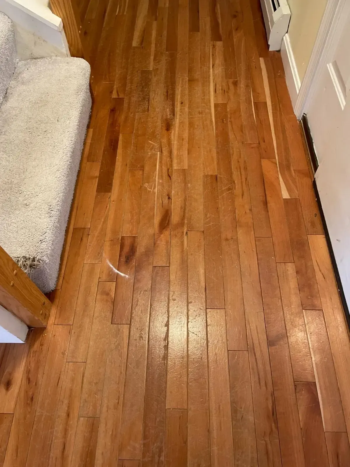 A wooden floor in a hallway with a couch and stairs.