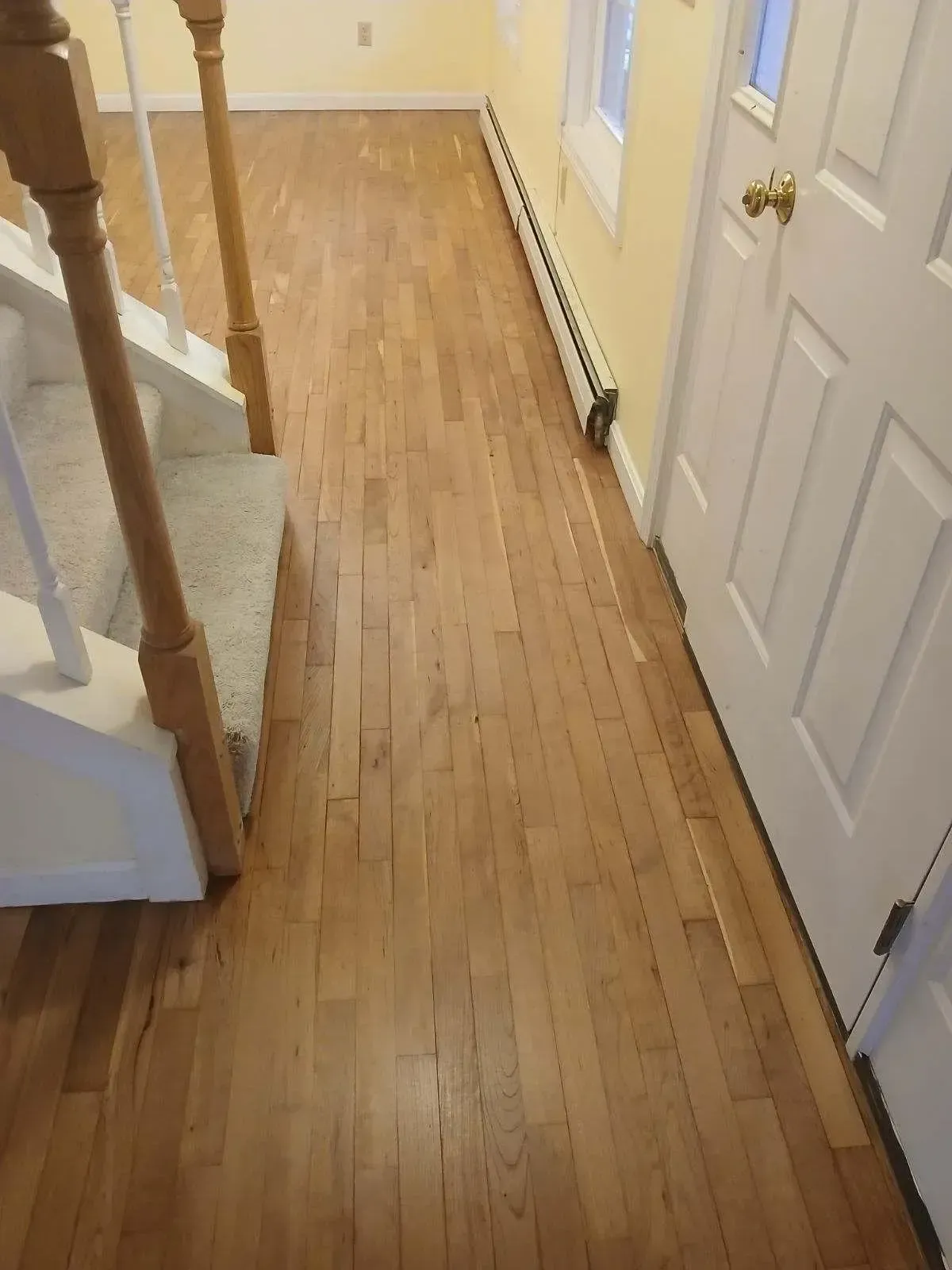 A hallway with hardwood floors and stairs in a house.