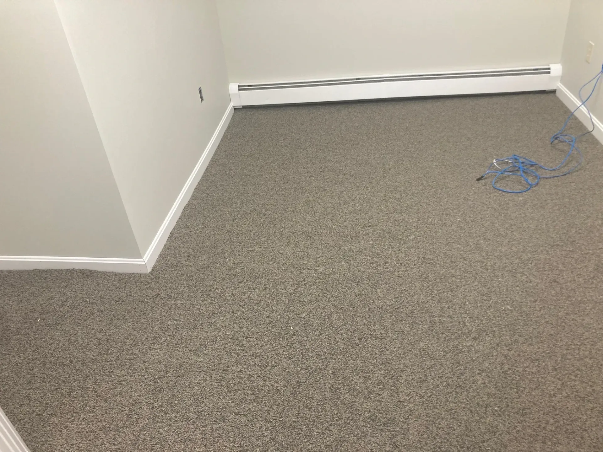 A room with a carpeted floor and a wall heater.