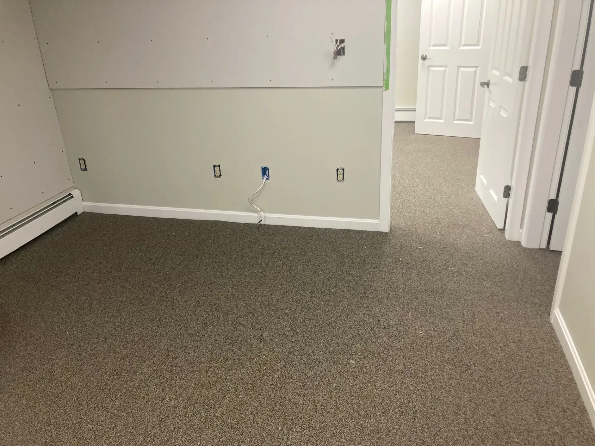 An empty room with a carpeted floor and a white wall.