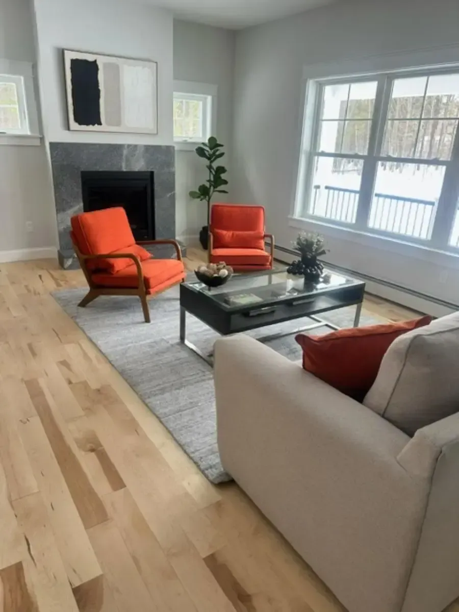 Living room with orange chairs, gray rug, white sofa, and a fireplace with artwork.