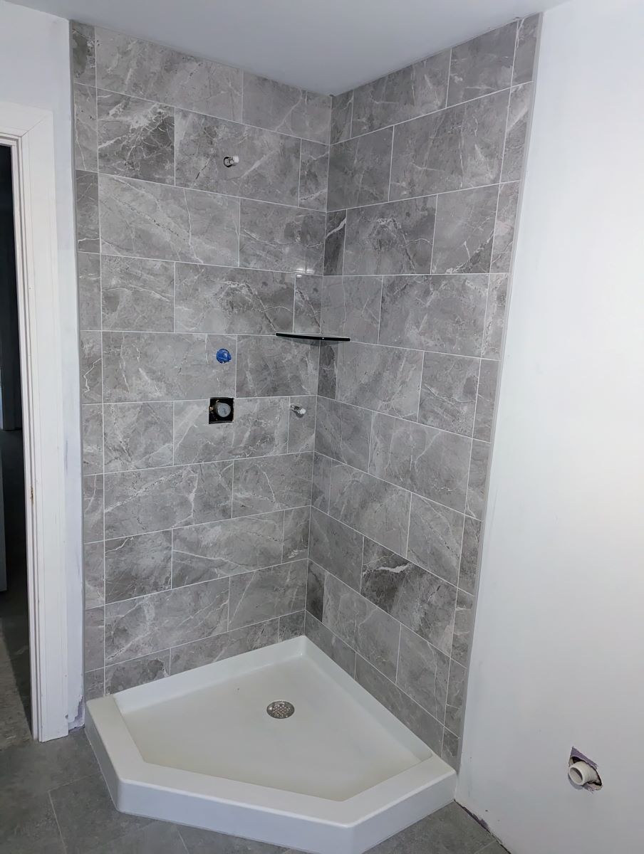 A shower stall in a bathroom with gray tiles on the wall.