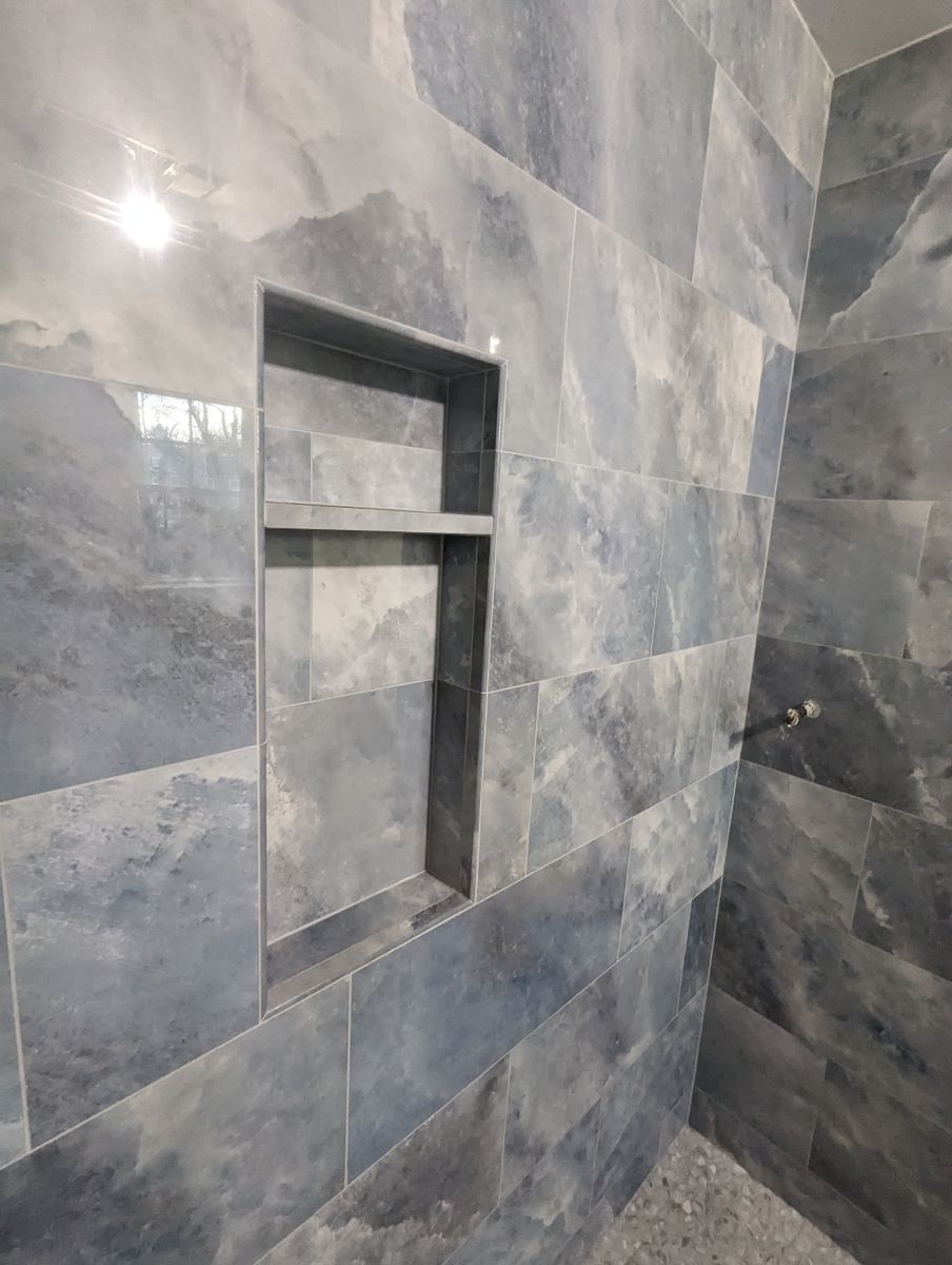 A bathroom with a shower stall and a shelf in the wall.