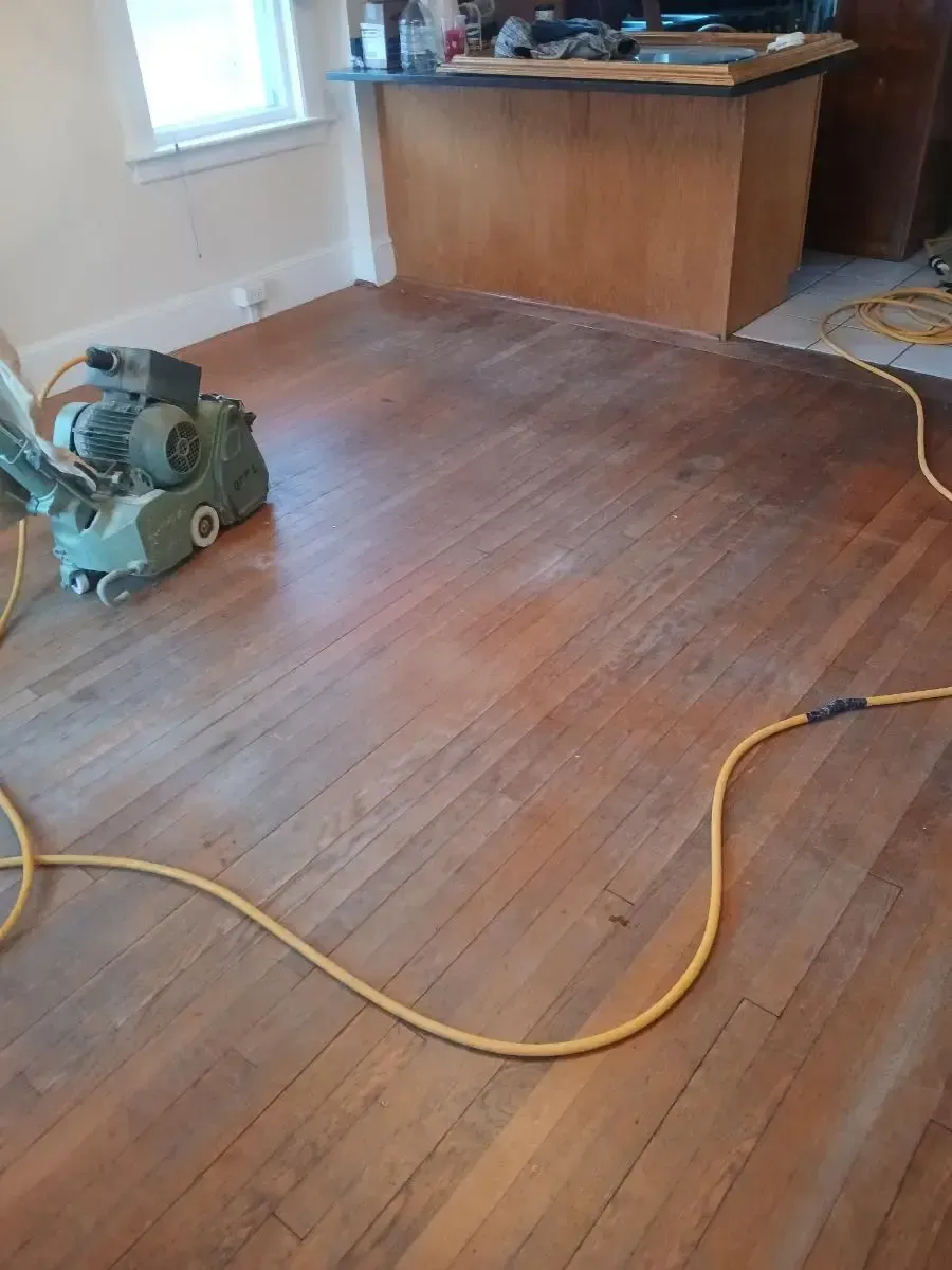Floor sanding machine on a wood floor in a room, with a countertop in the background.