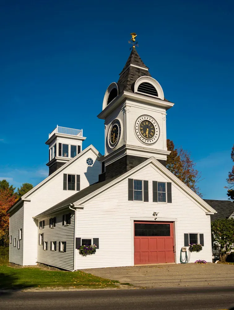 White church with a clock tower, red doors, and a gold steeple under a clear blue sky.