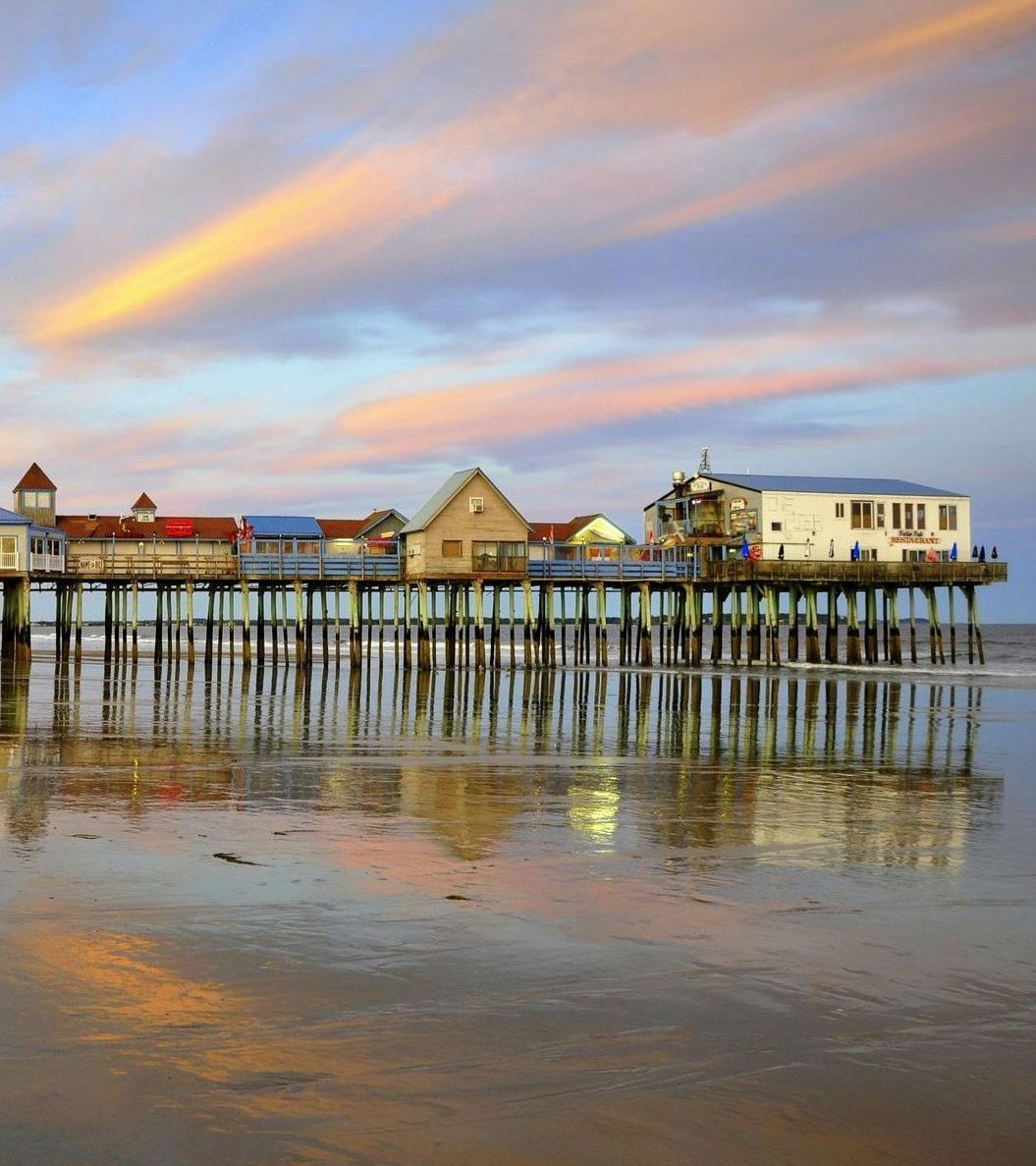 A pier sitting on top of a sandy beach at sunset.