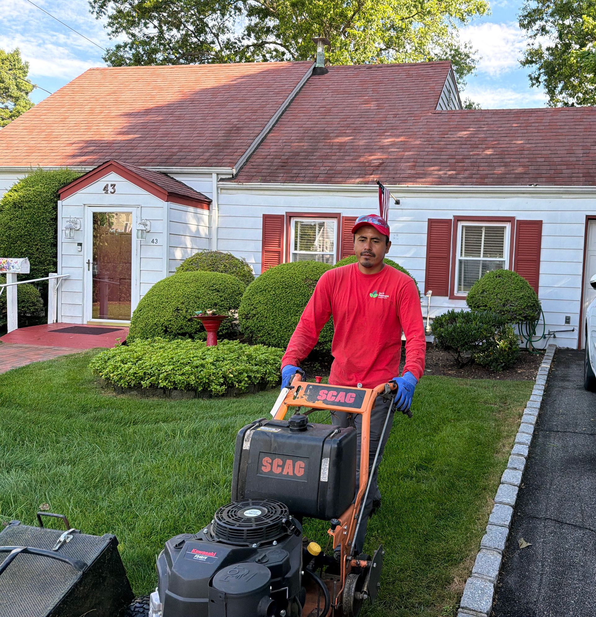 Worker in red shirt using a lawn mower on a suburban front yard