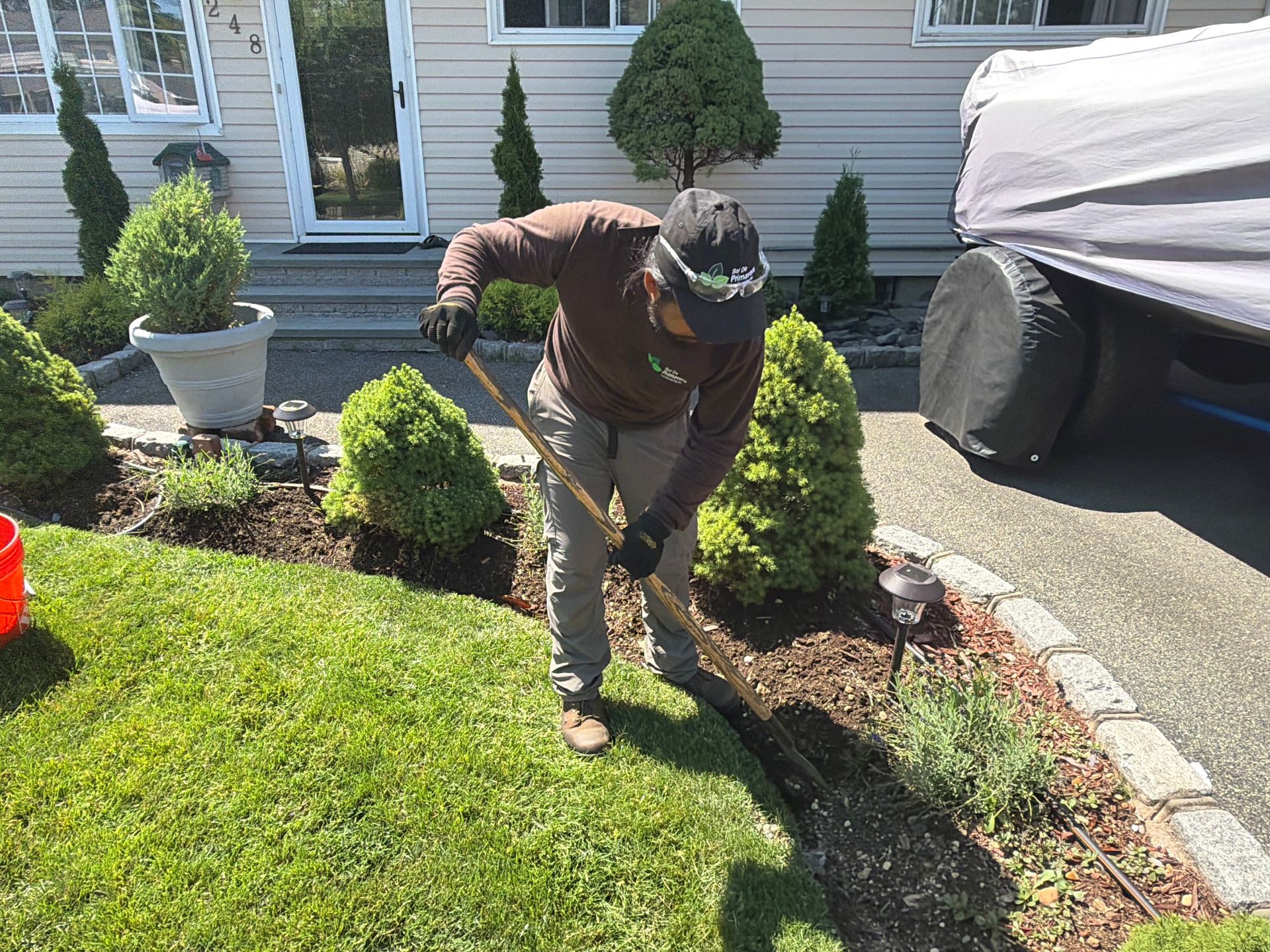 Person raking leaves beside a house, near a driveway and landscaped front yard.
