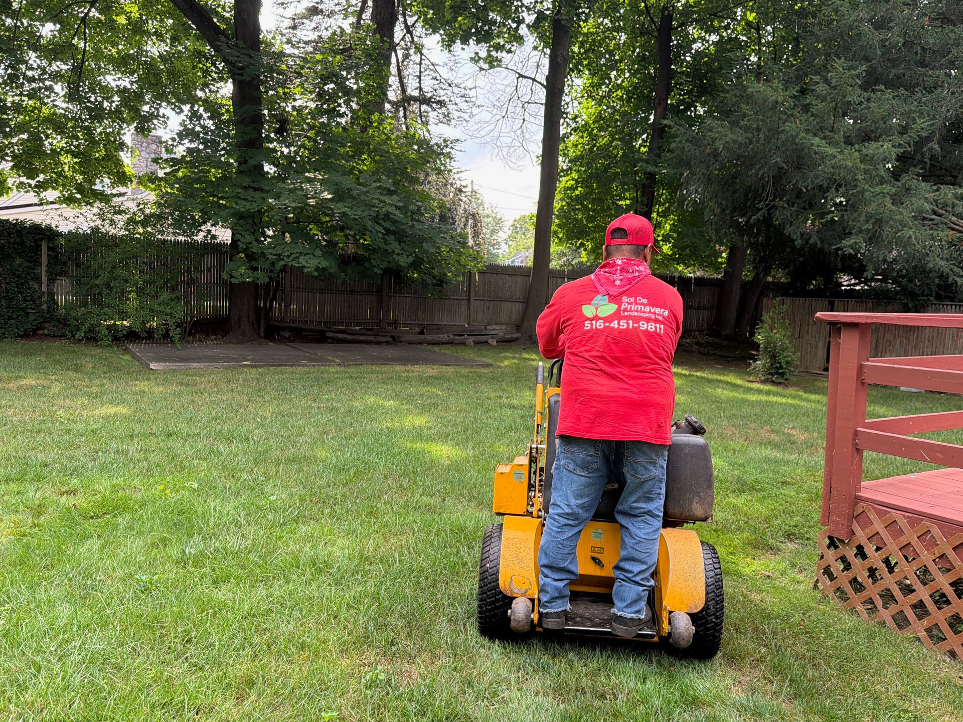 Person in red shirt operating a yellow lawn mower in a grassy backyard.