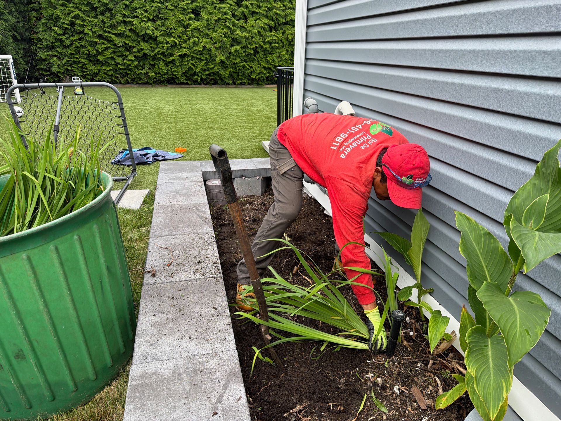 Person in red jacket planting in a garden bed beside a house and walkway
