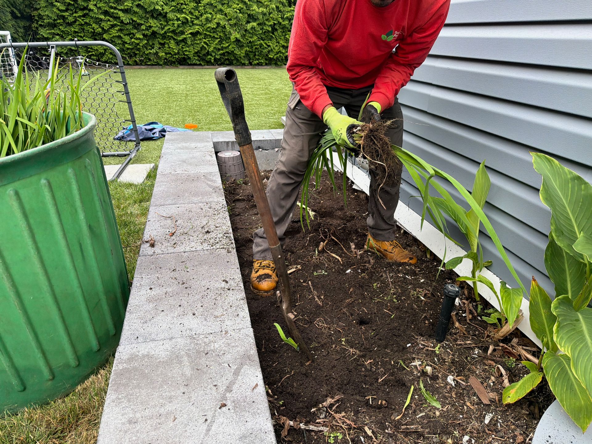 Person planting seedlings in a garden bed beside a house and green planter
