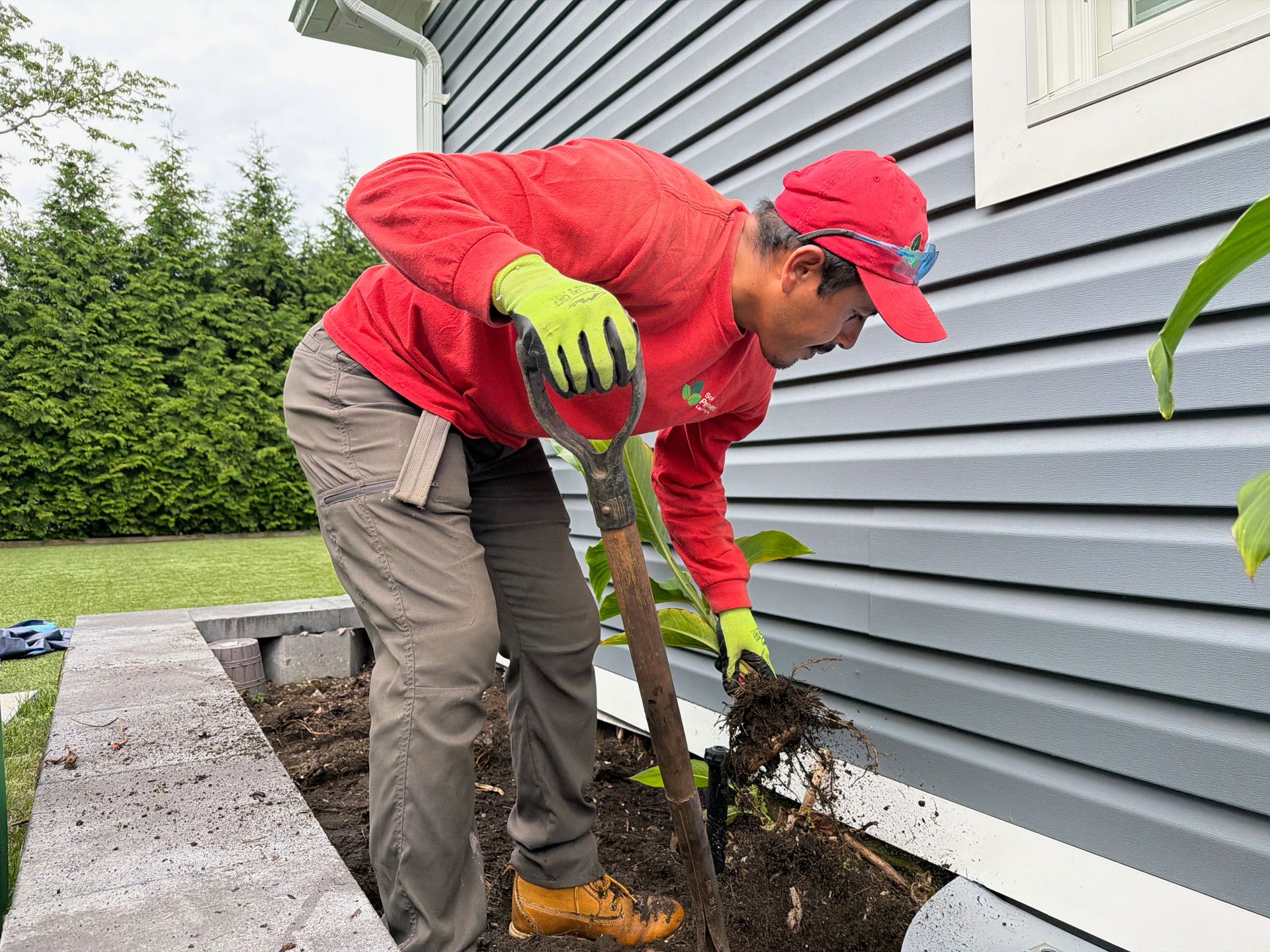 Person in red jacket planting in a garden bed beside a house