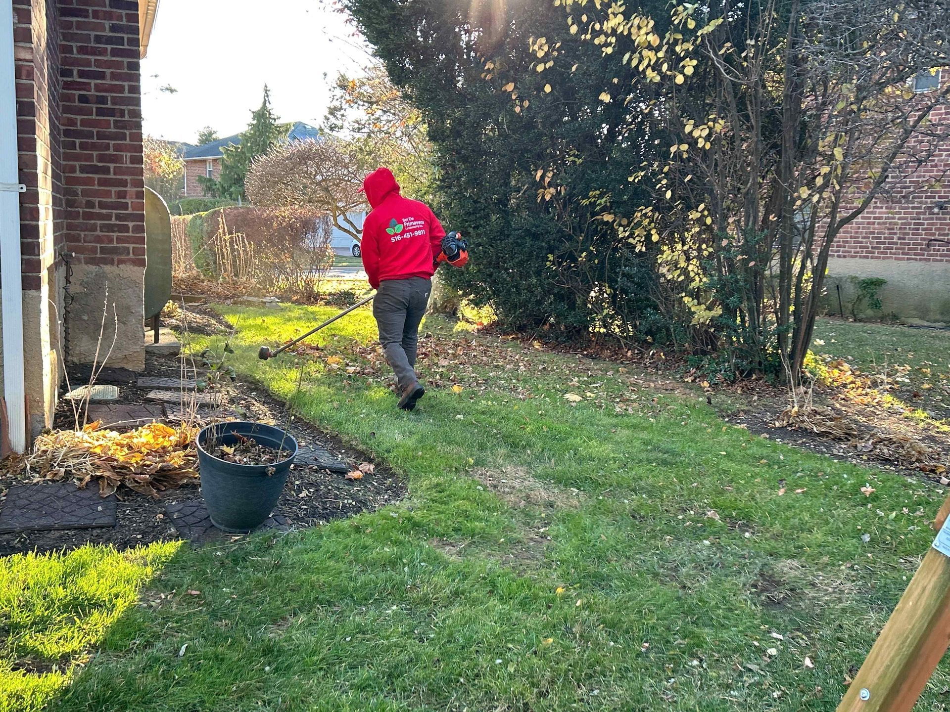 Person in a red jacket walking across a grassy backyard beside a brick house and trees.