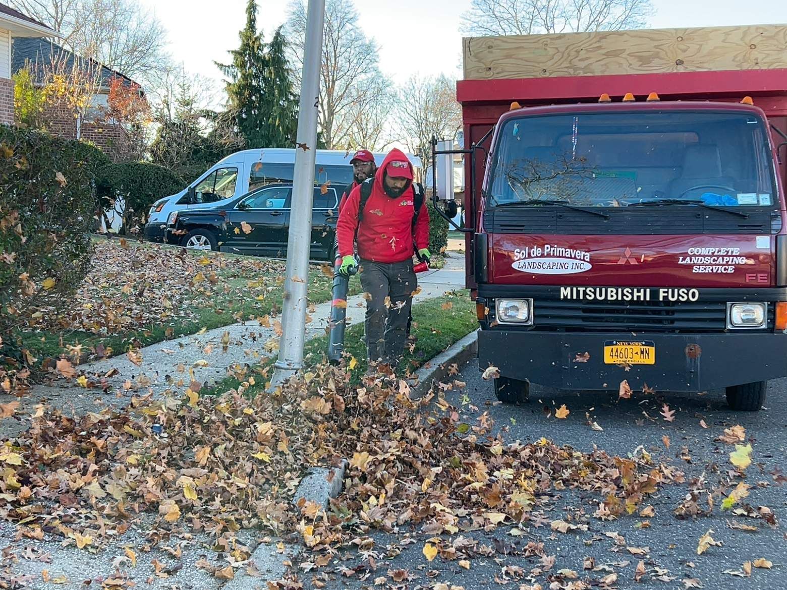 Person in red jacket standing by a red truck on a leaf-covered street