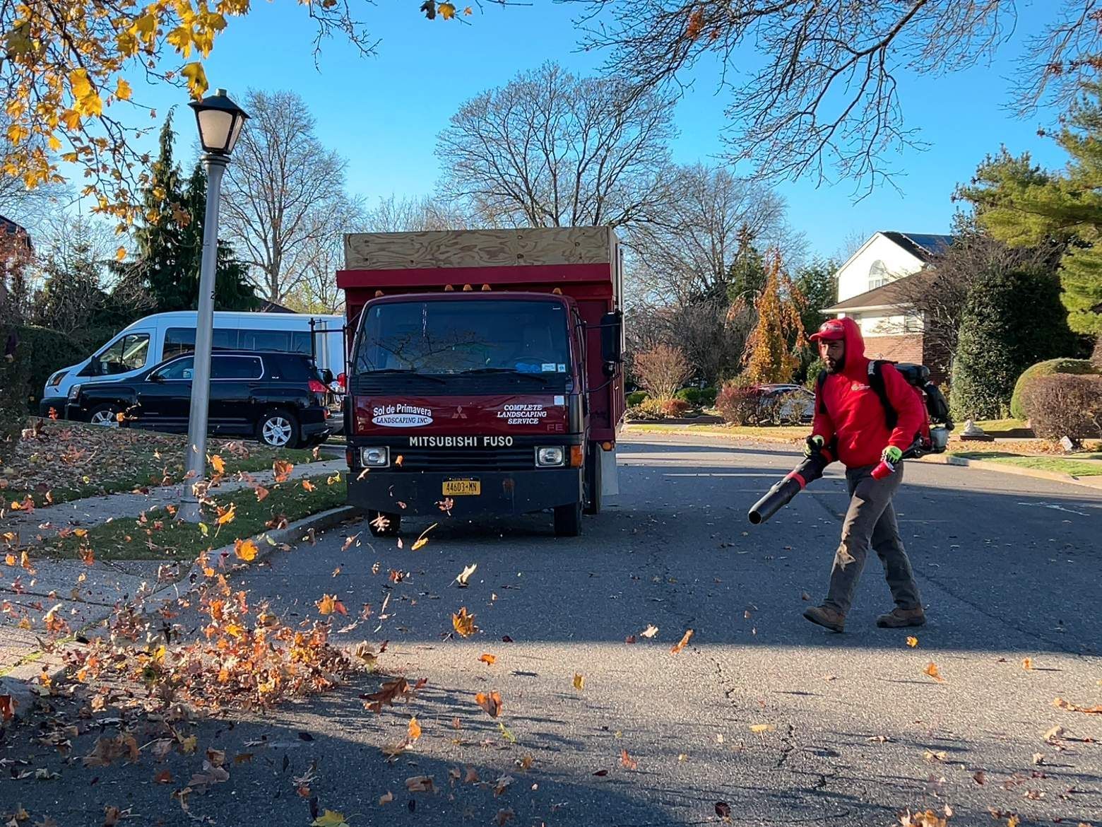 Person raking leaves beside a red truck on a suburban street in autumn