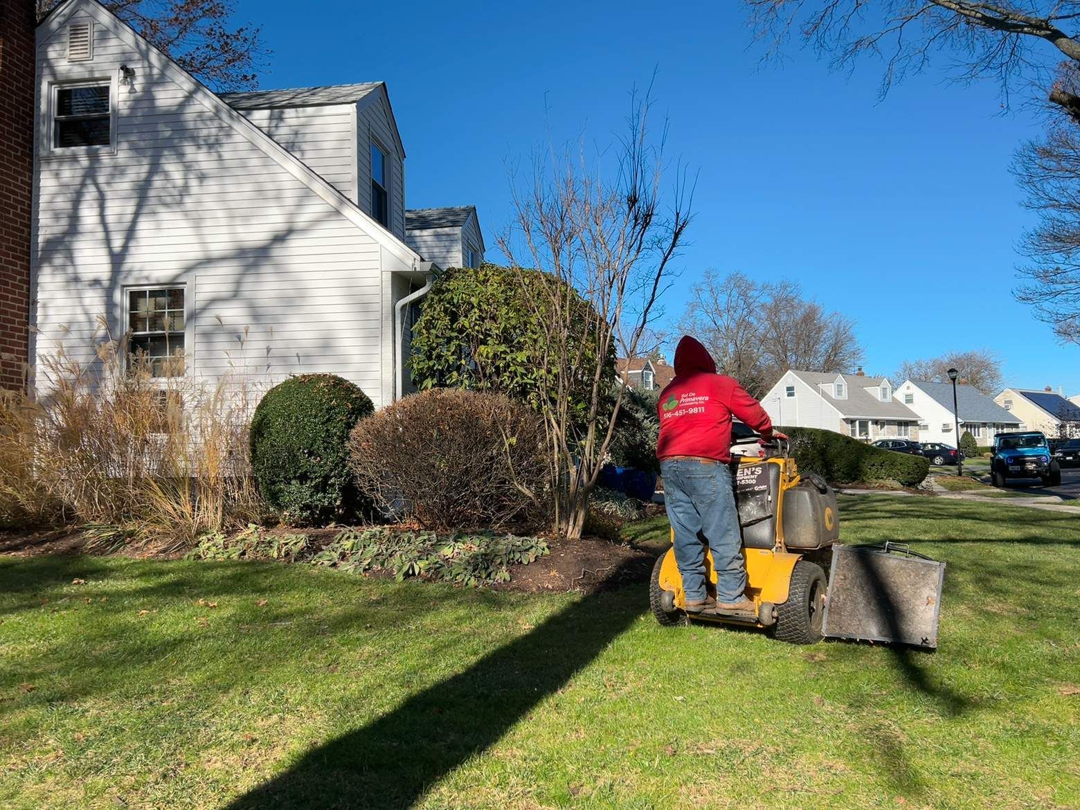 Person mowing a lawn beside a white house on a sunny day