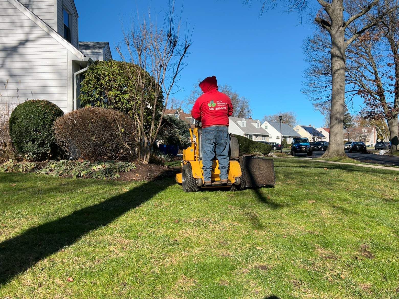 Person mowing a lawn with a yellow riding mower beside a house on a sunny day