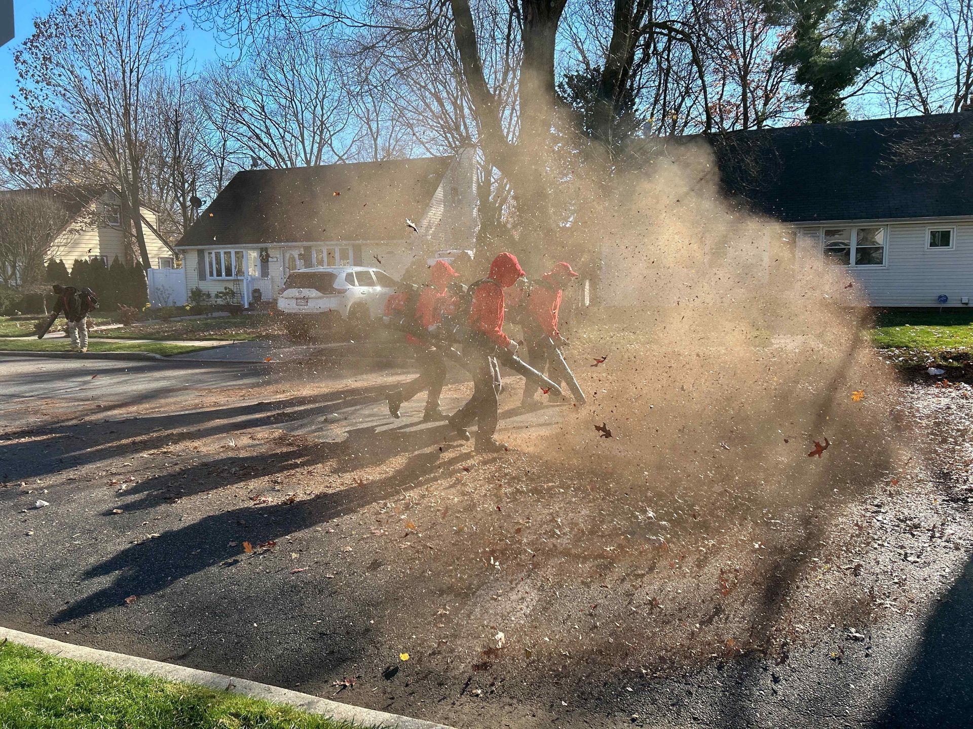 People kicking up a large cloud of dust on a sunny residential street near houses