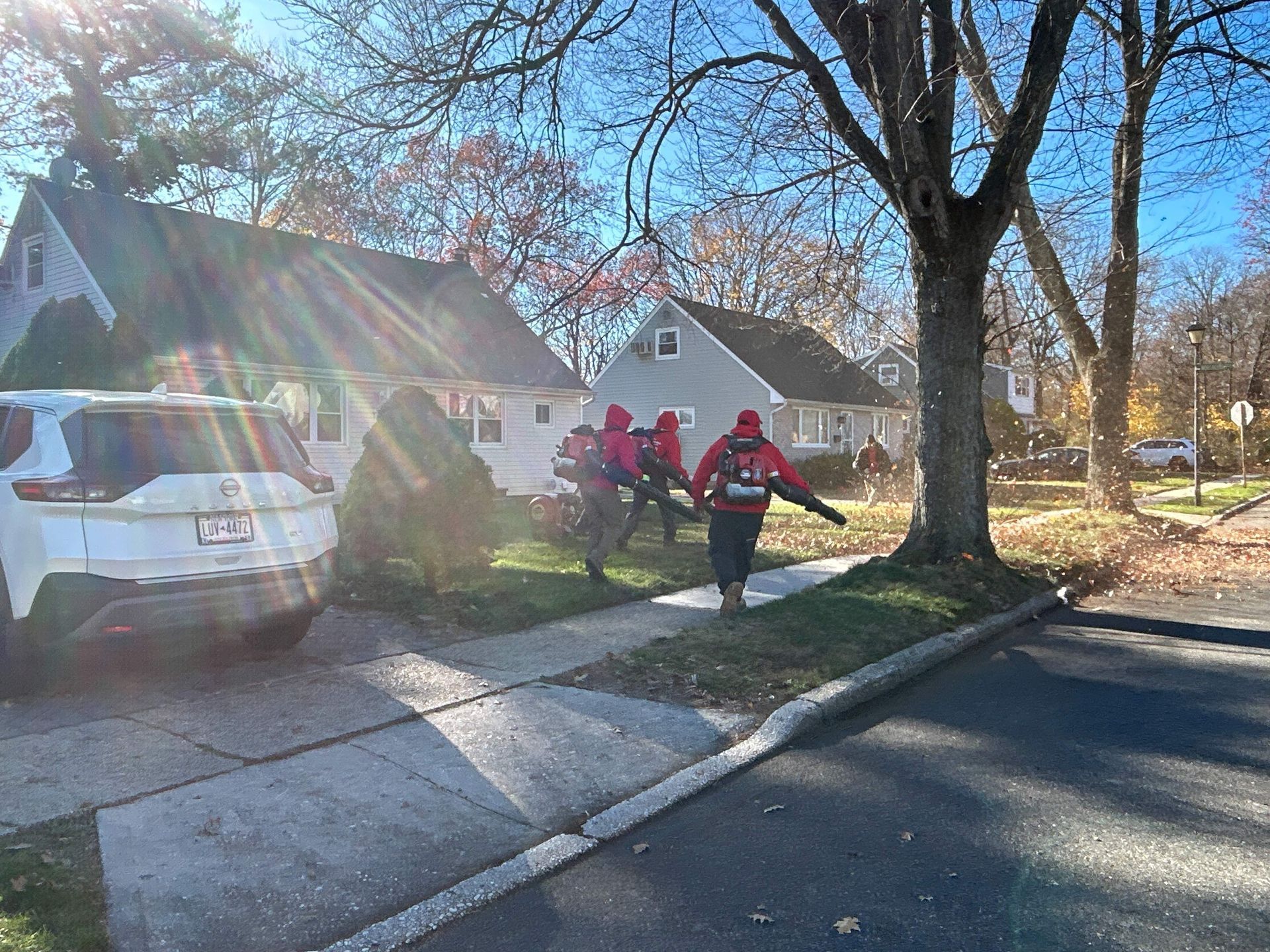Firefighters walking with hoses beside a house on a sunny residential street