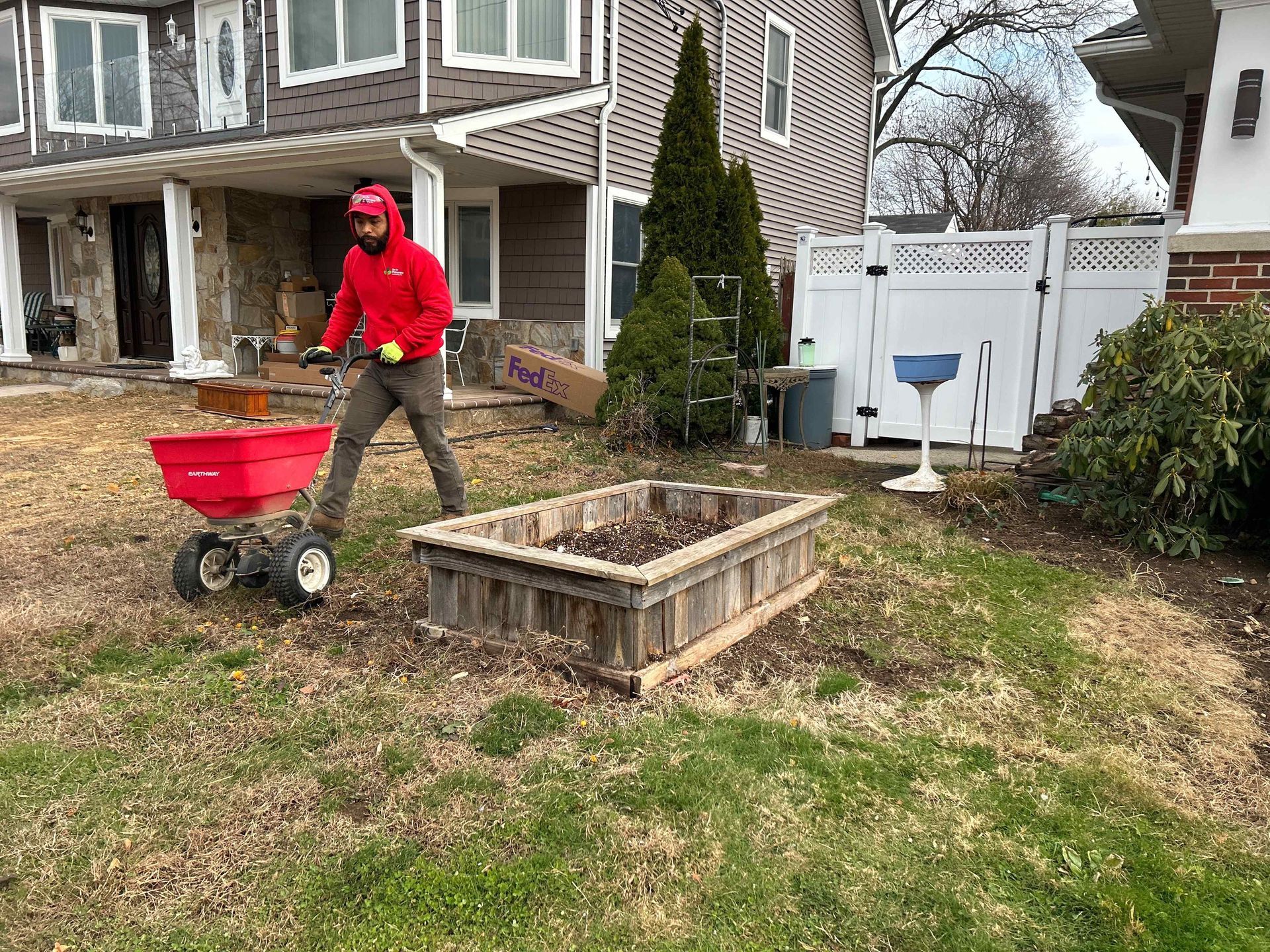 Person in red hoodie pushing a red cart in a yard beside a raised garden bed.