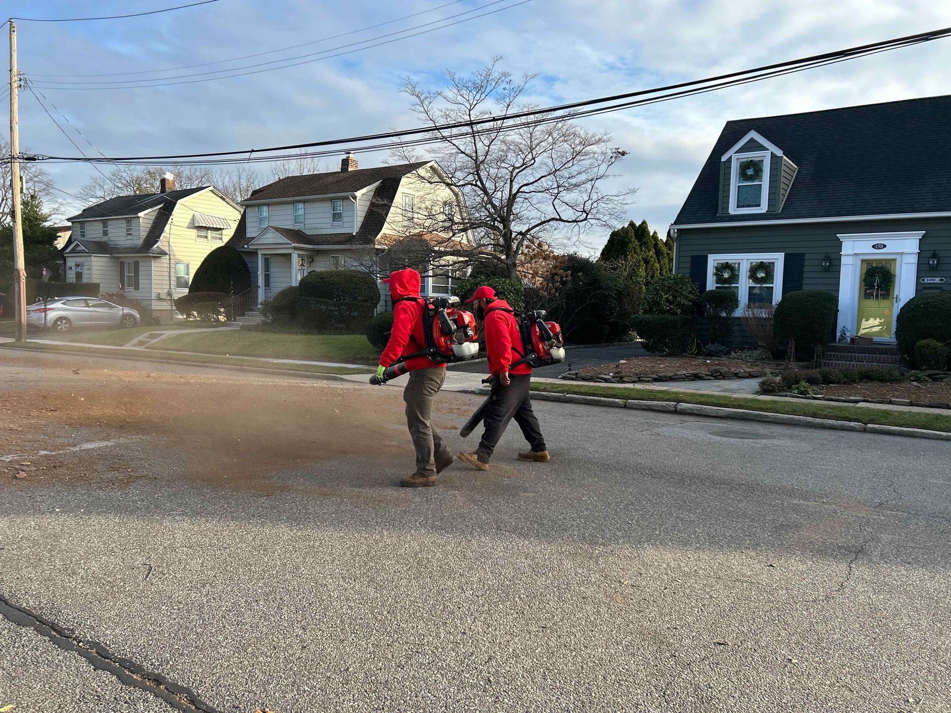 Two workers in red safety gear spraying mist on a residential street near houses