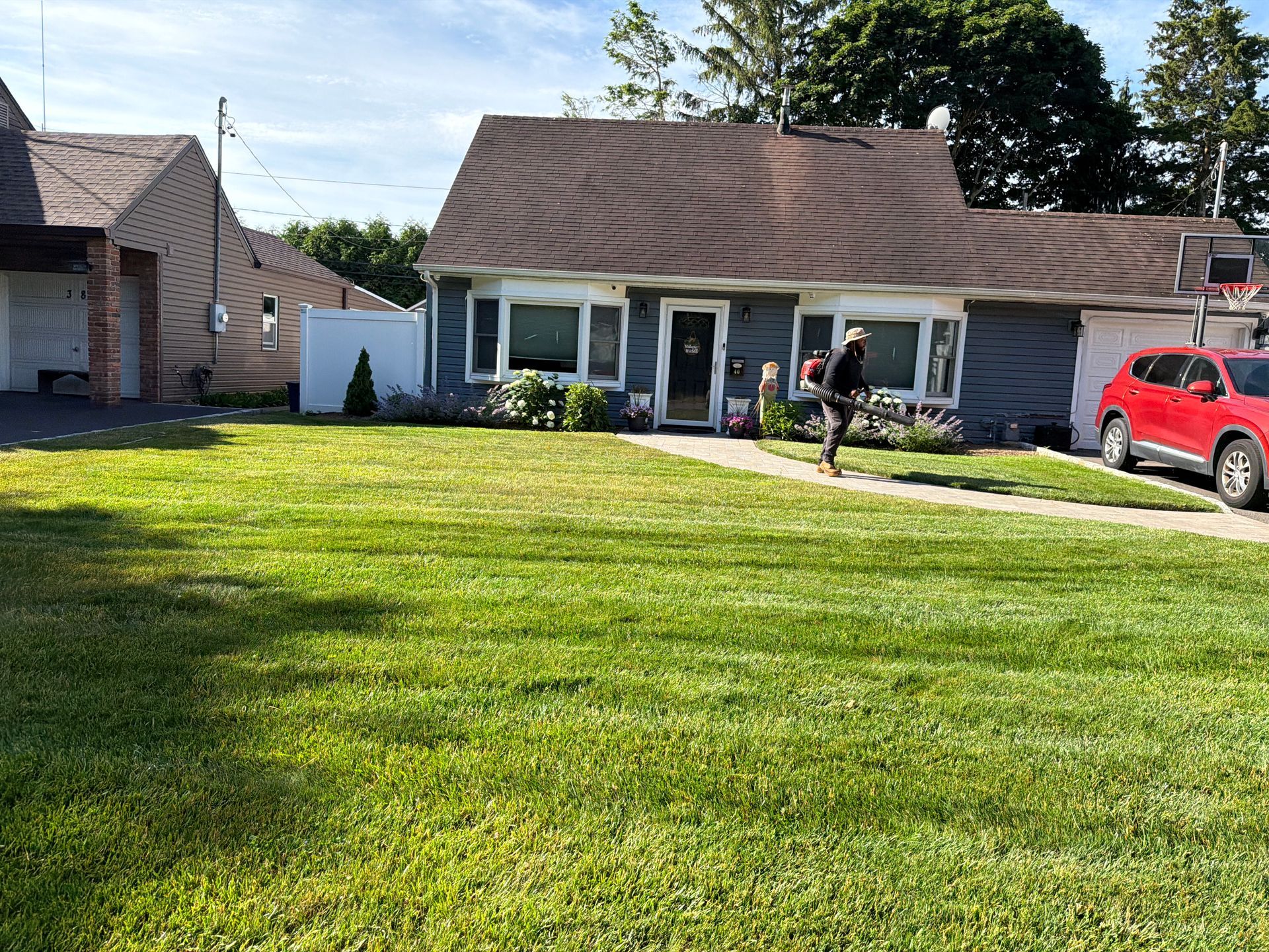Suburban house with a large green lawn, a person on the porch, and a red car in the driveway