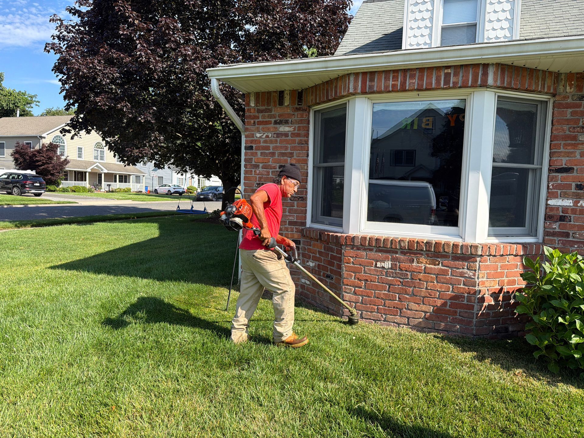 Worker using a string trimmer on a brick house lawn in a suburban yard