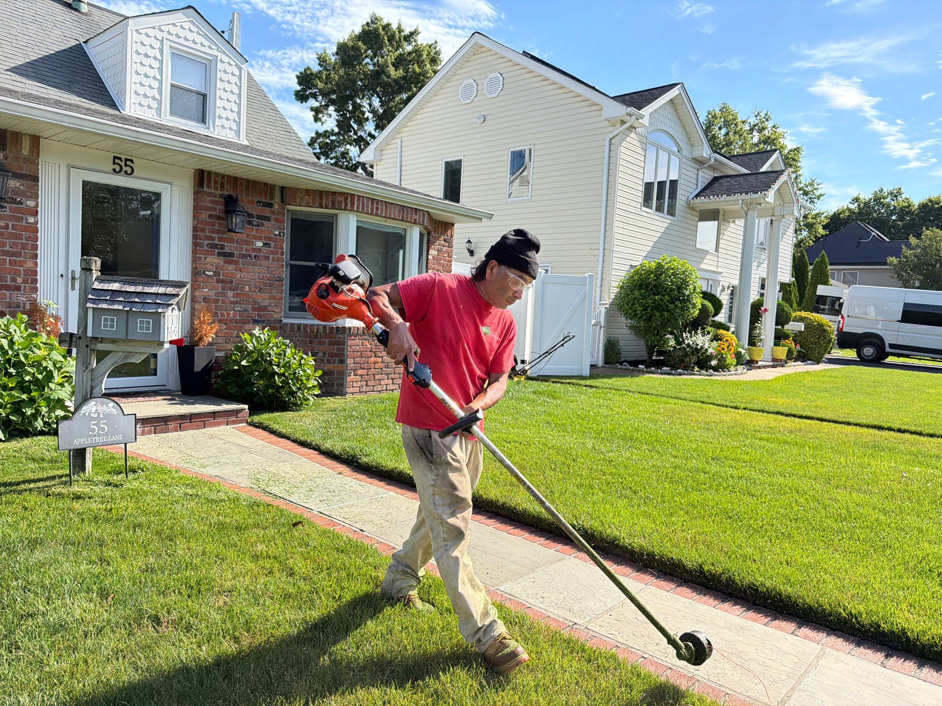 Person mowing a suburban lawn beside a brick house and white garage on a sunny day