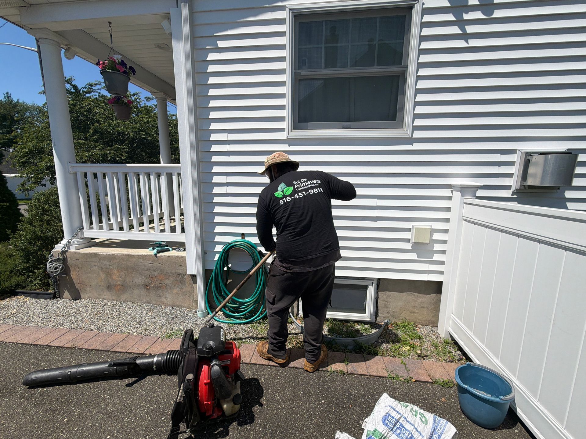 Worker cleaning exterior siding beside a white house with a pressure washer and hose