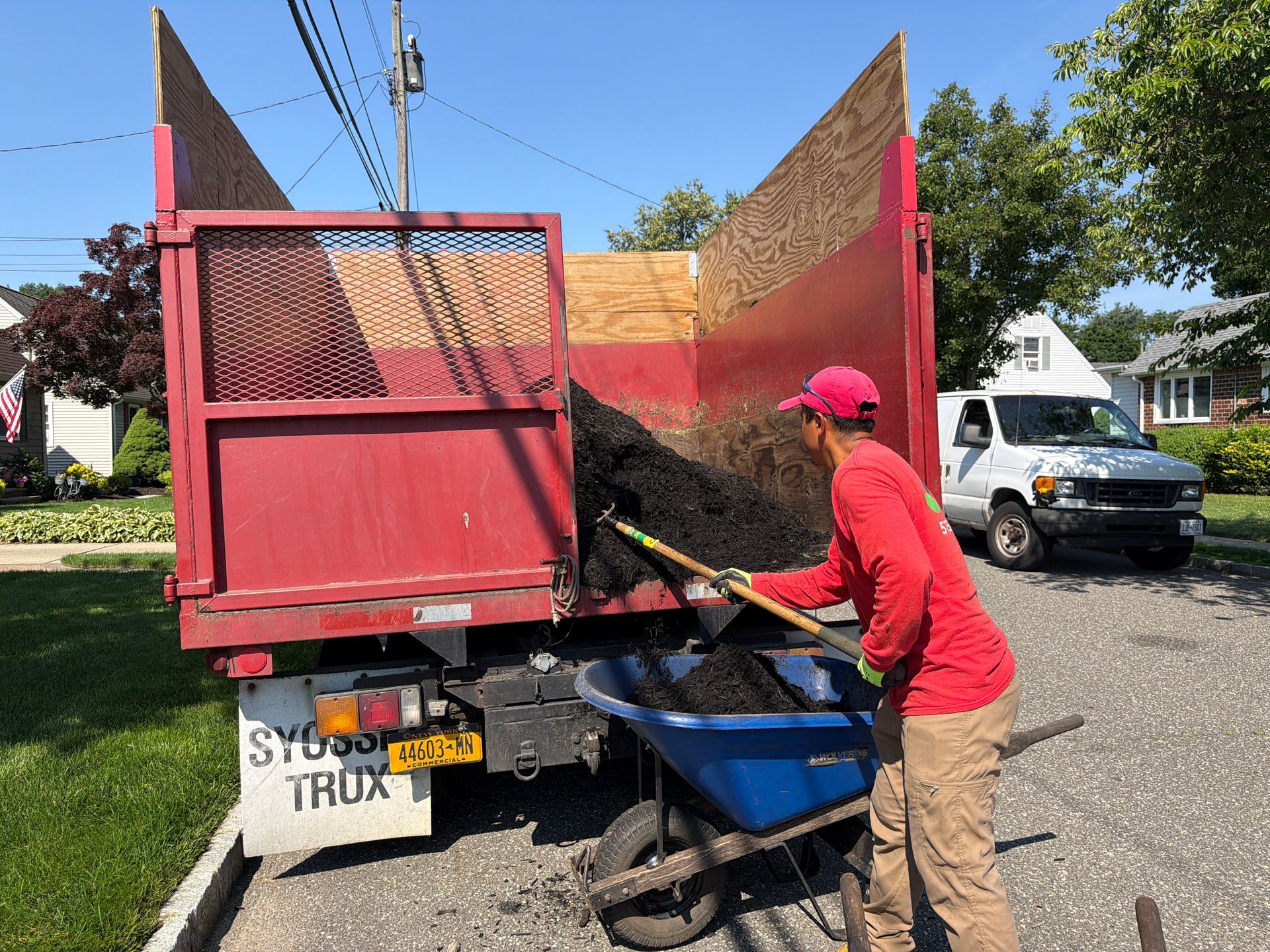Worker in red shirt loading debris into a red truck with a blue cart on a suburban street