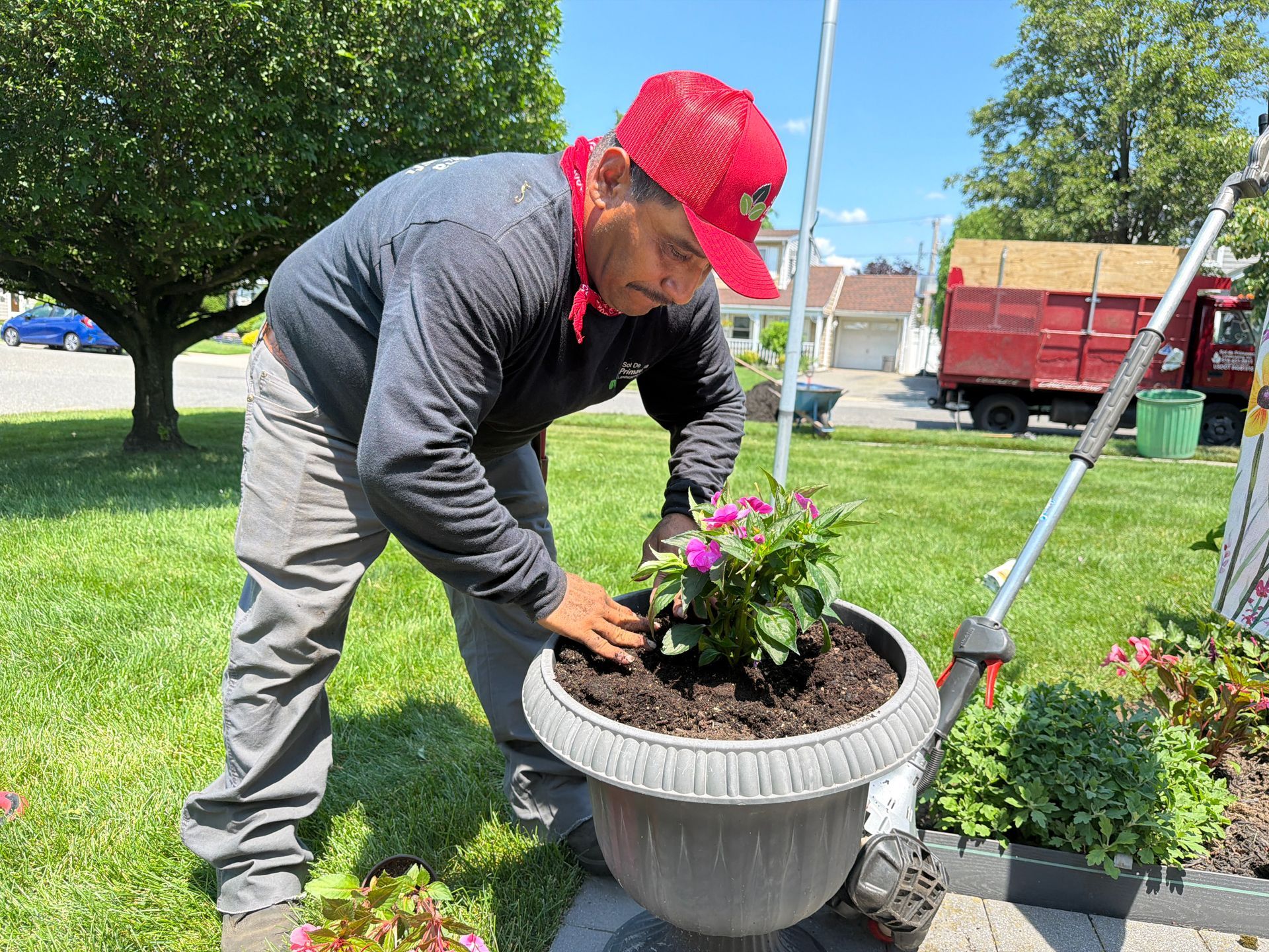 Person planting flowers in a gray planter outdoors on a sunny lawn.