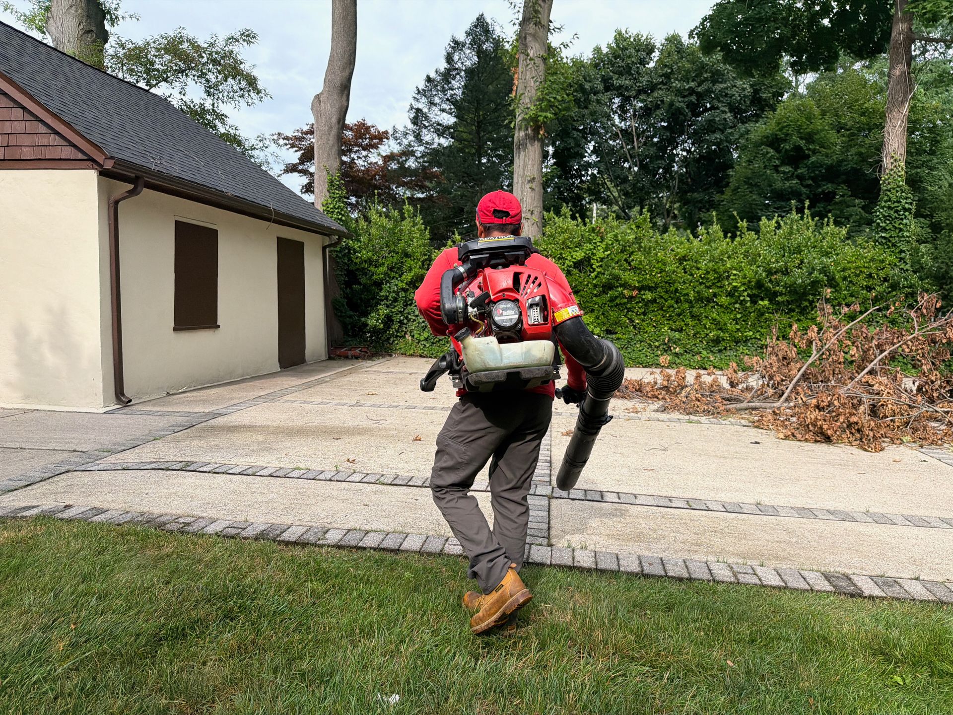 Rescuer in red gear carrying a person across a gravel path beside a house and trees
