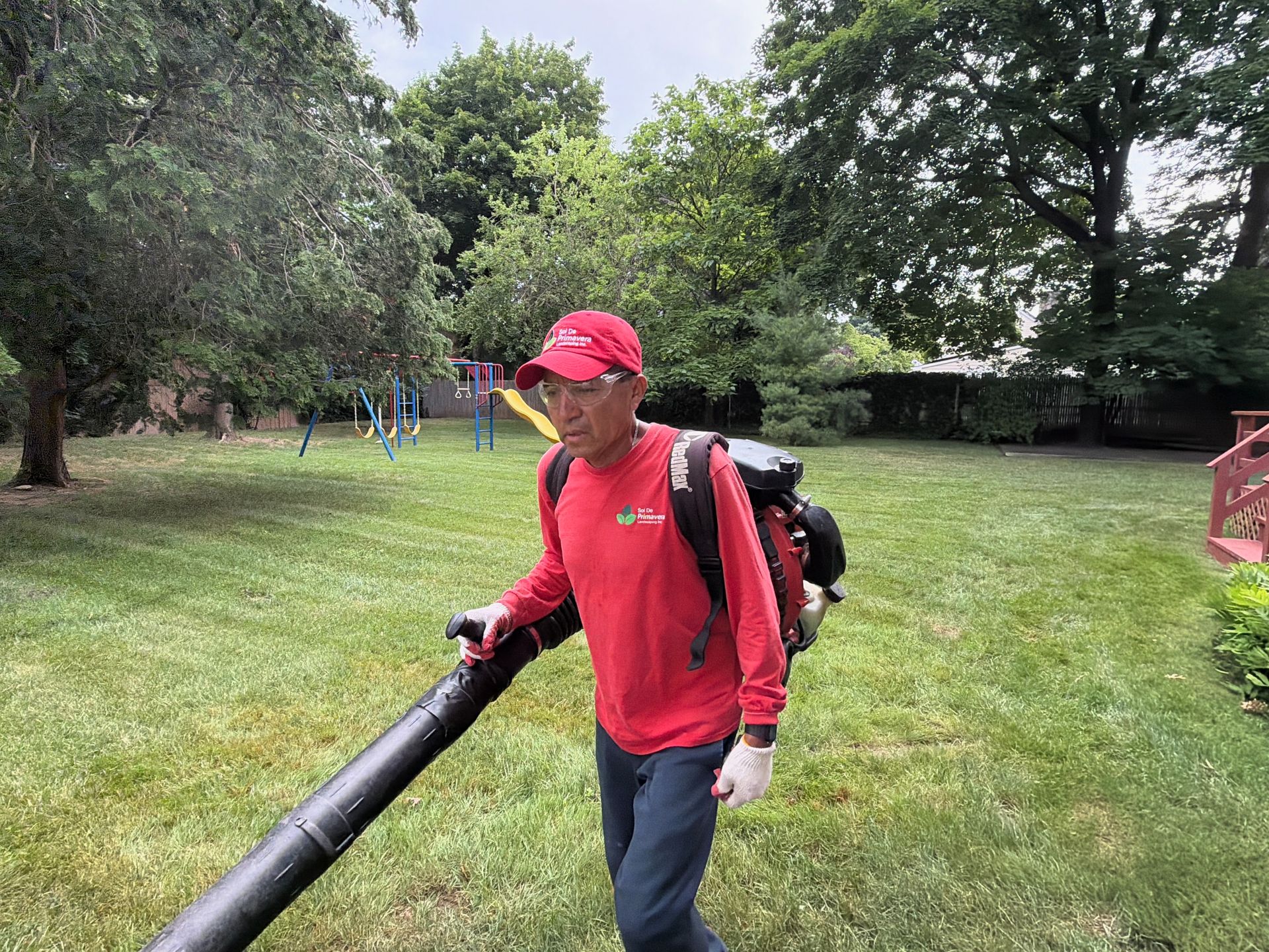 Person in red jacket and cap carrying a long black pipe in a grassy park.