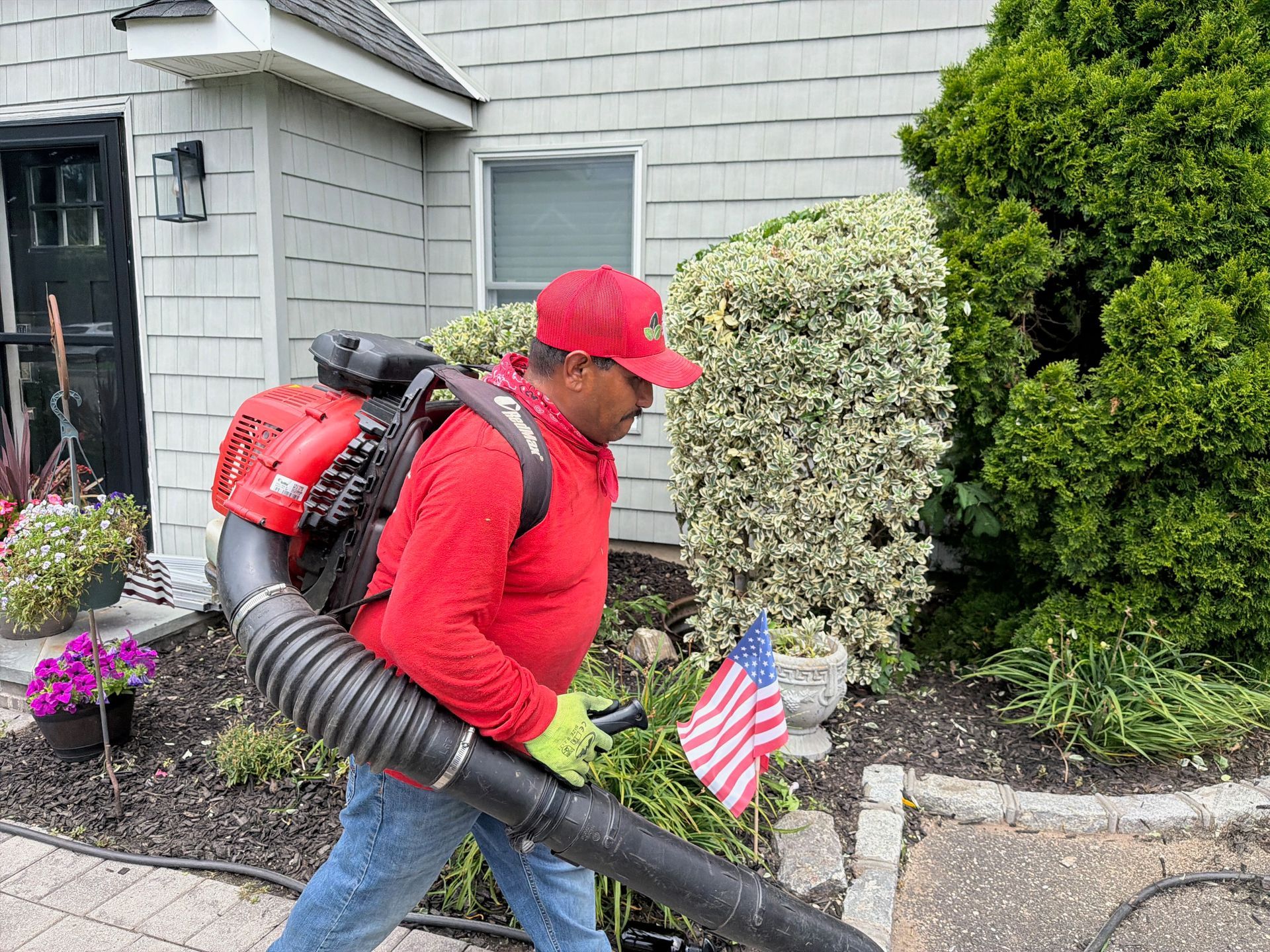 Worker using a backpack leaf blower beside a house and garden path