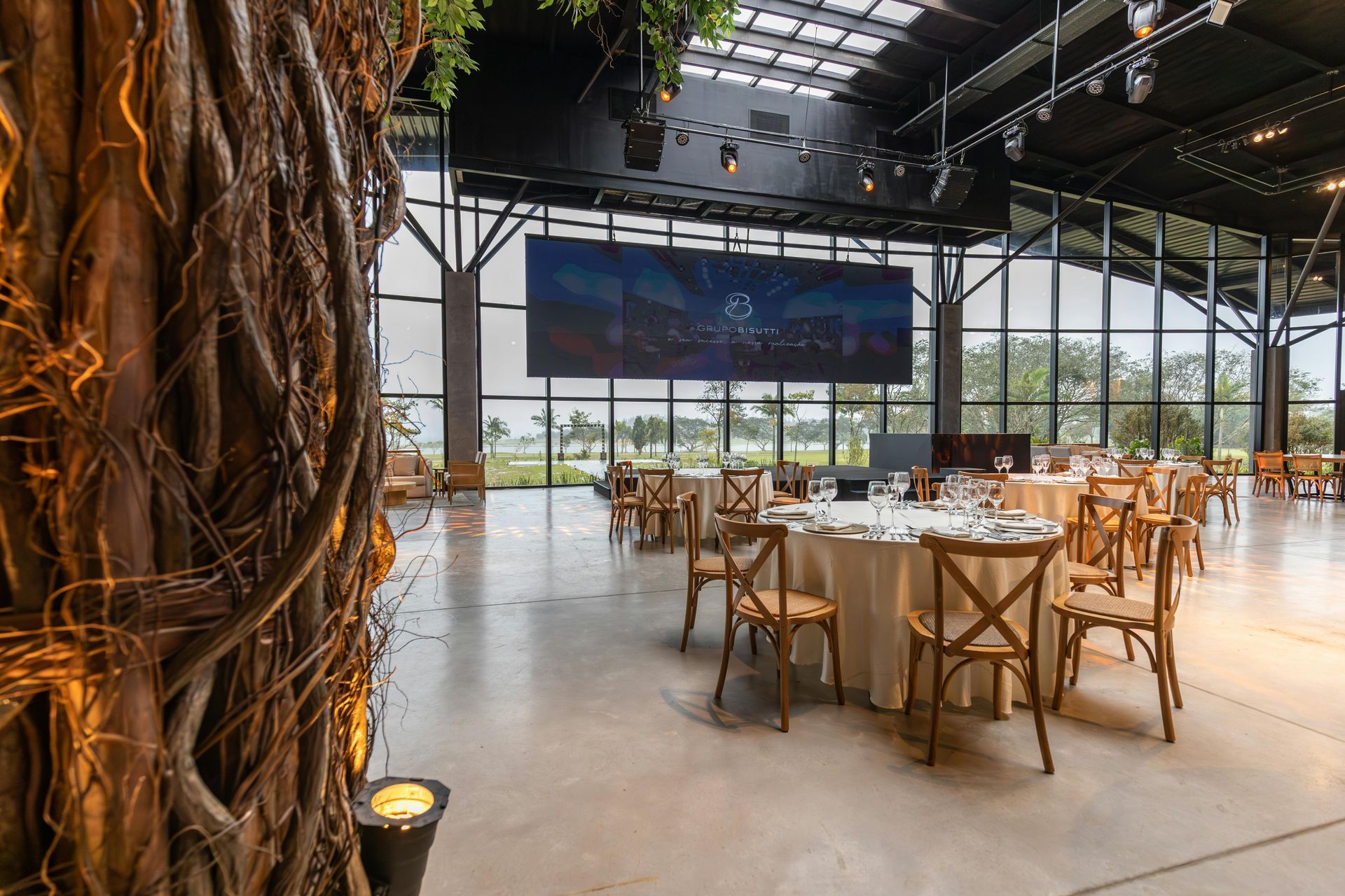 A large room with tables and chairs and a tree in the background.