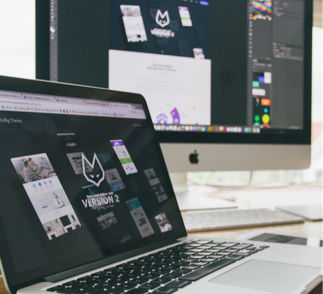 A laptop computer is open on a desk next to two monitors.
