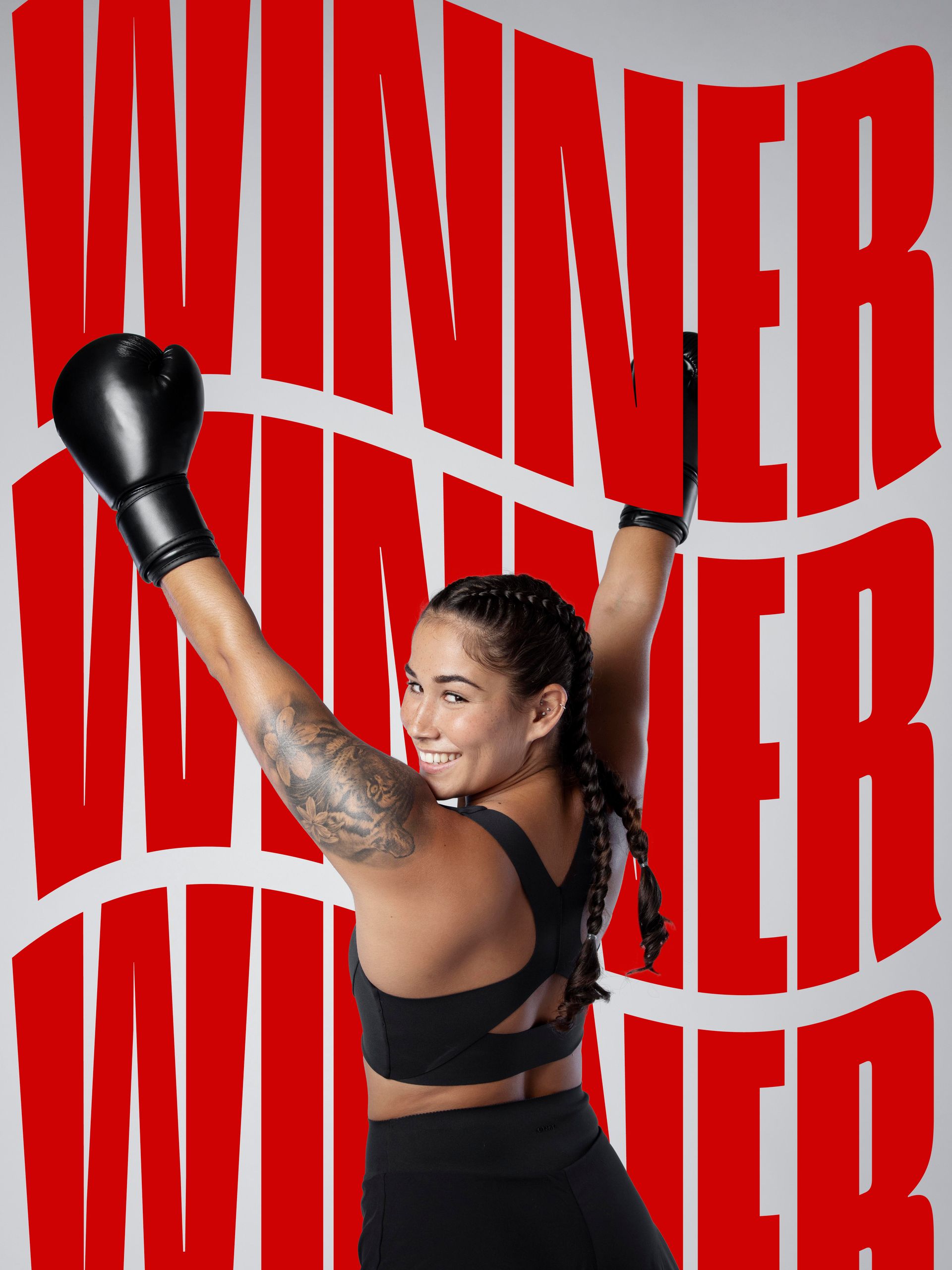 A woman wearing boxing gloves is standing in front of a poster that says `` winner ''.