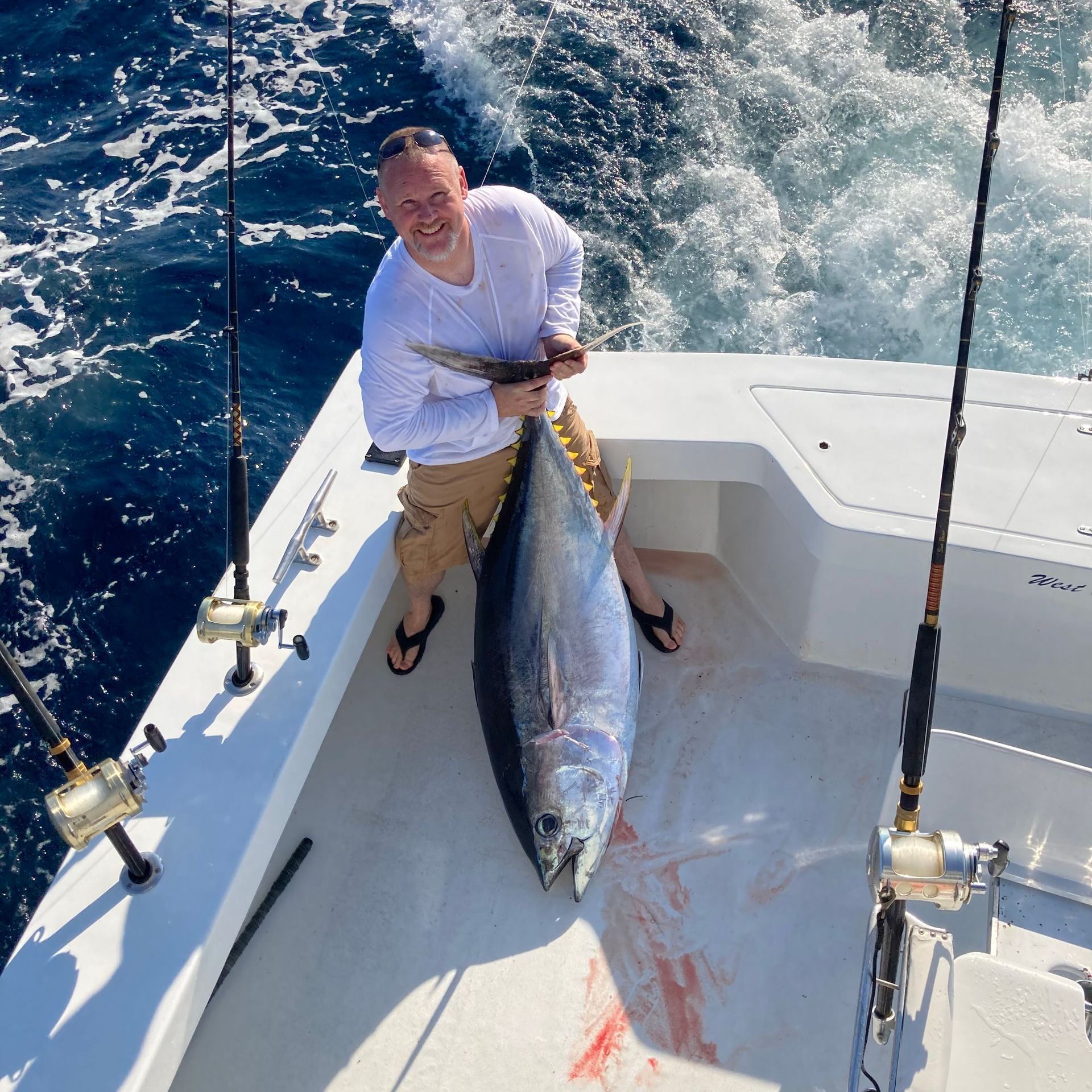 Man on boat holding a large tuna fish, ocean water.