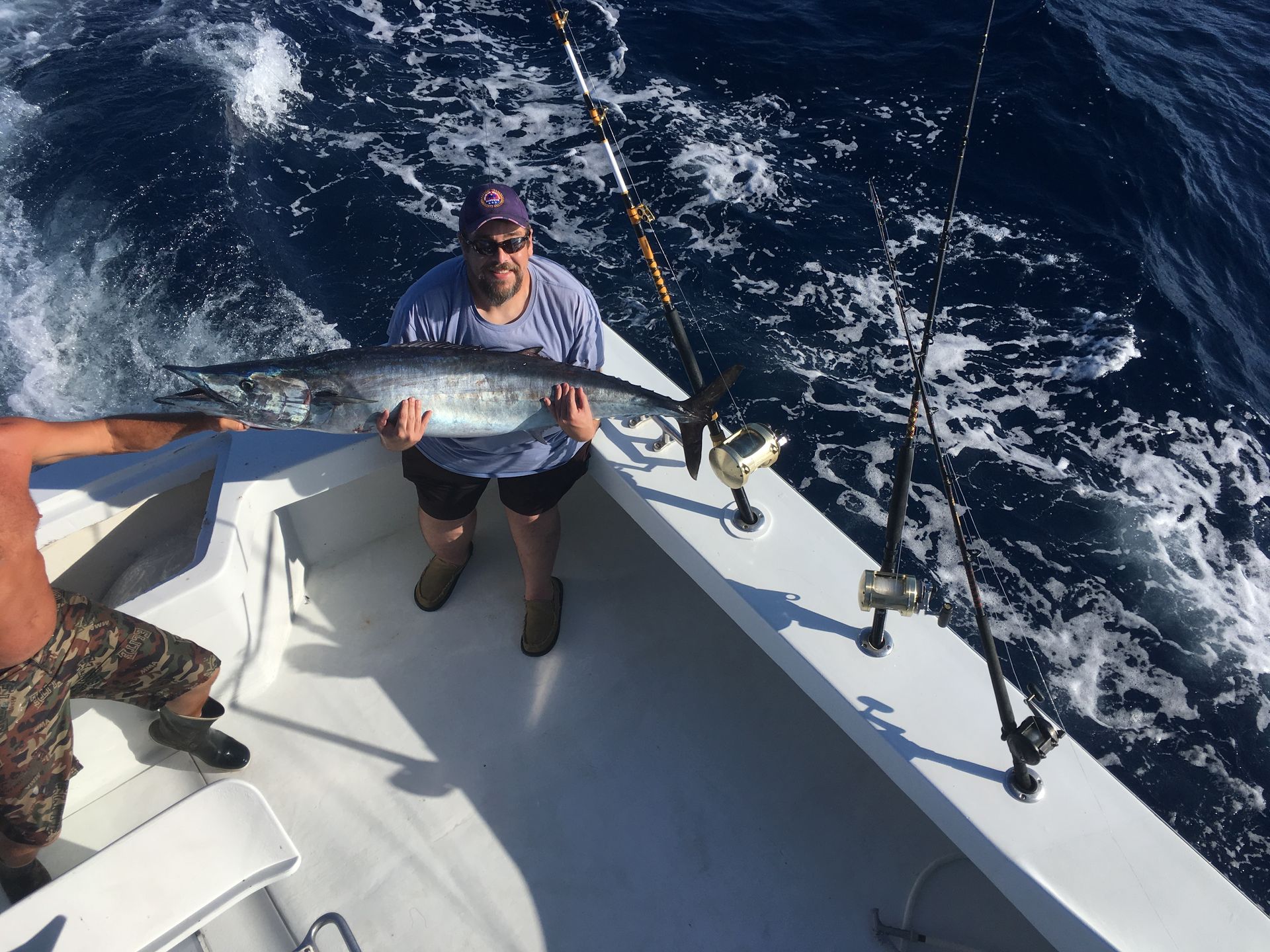Man on boat holding large fish; ocean setting with fishing rods.