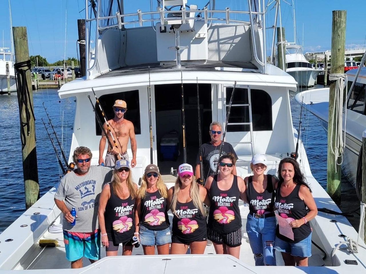 Group of people posing on a boat, some wearing matching shirts. Sunny outdoor setting.