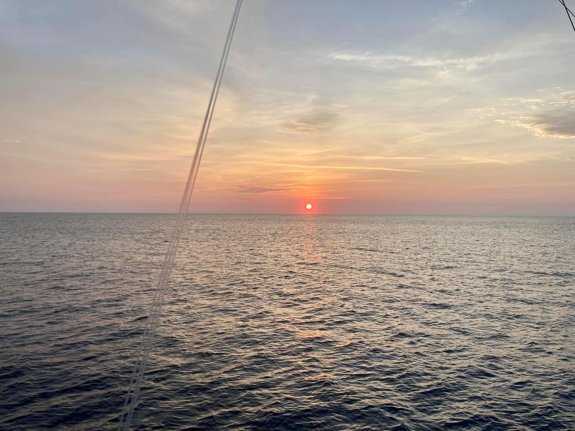 Sunset over ocean, with the sun a fiery orange orb, reflecting on rippled water; pastel sky.