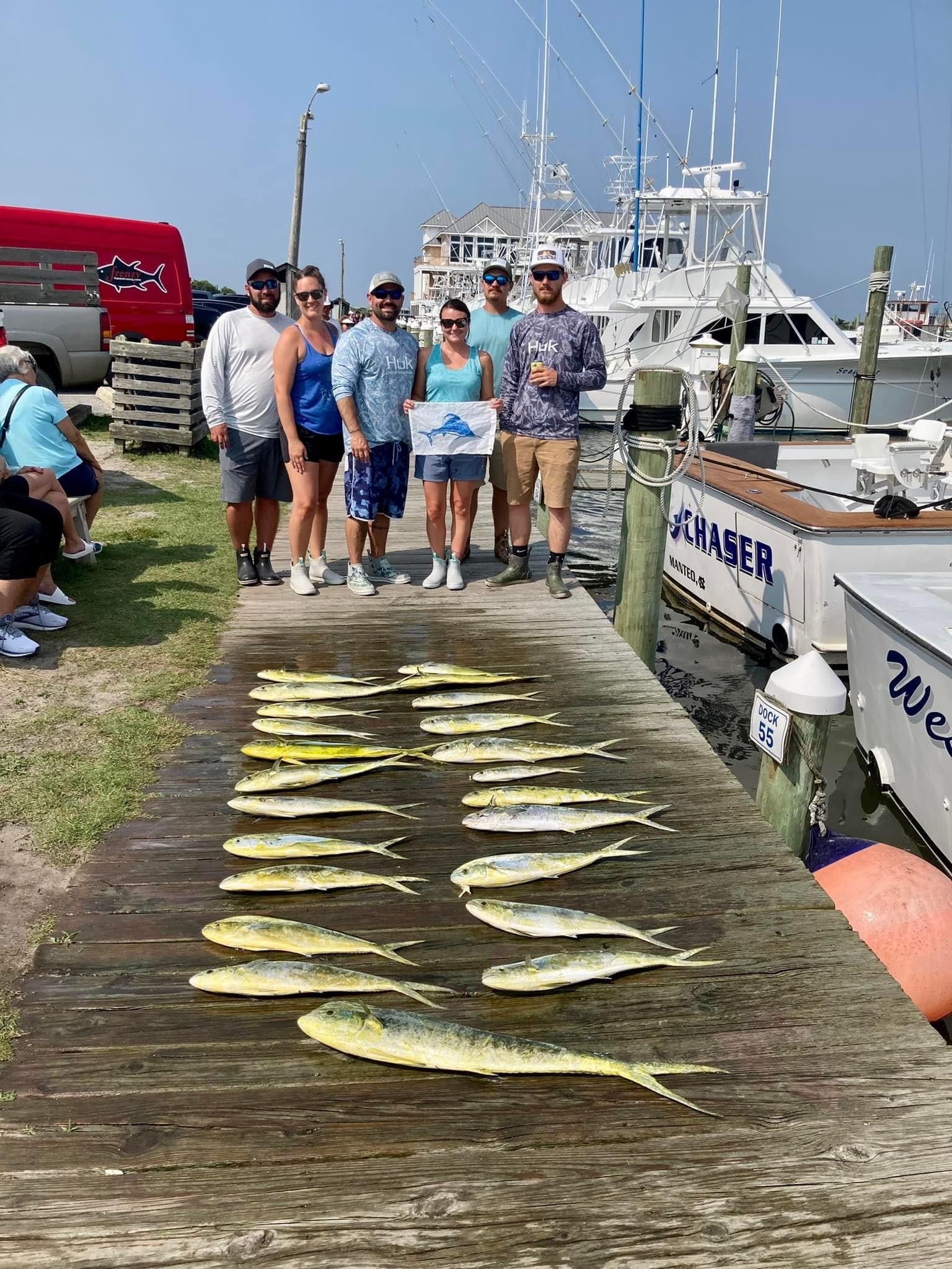 Group of people on a dock with a large catch of yellow fish. Boat in background.