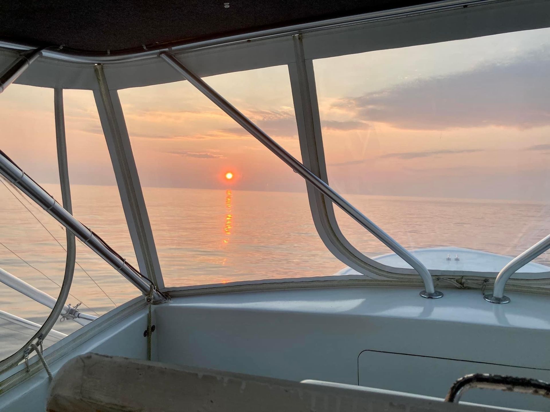 Sunset over calm water viewed from a boat's cabin, with orange and pink hues.