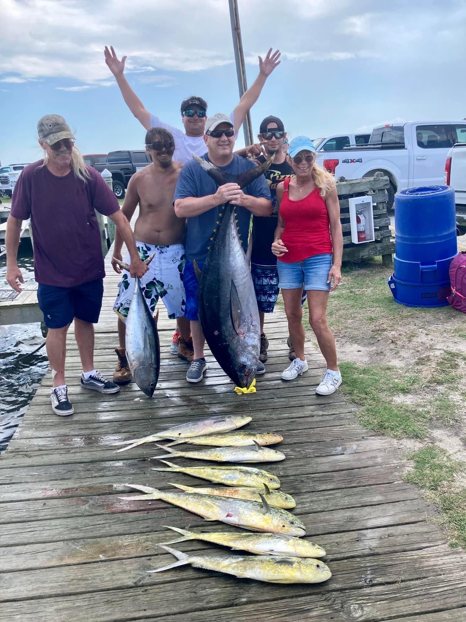 Group of people on a dock with a large fish and several smaller fish. People are smiling and holding up fish.