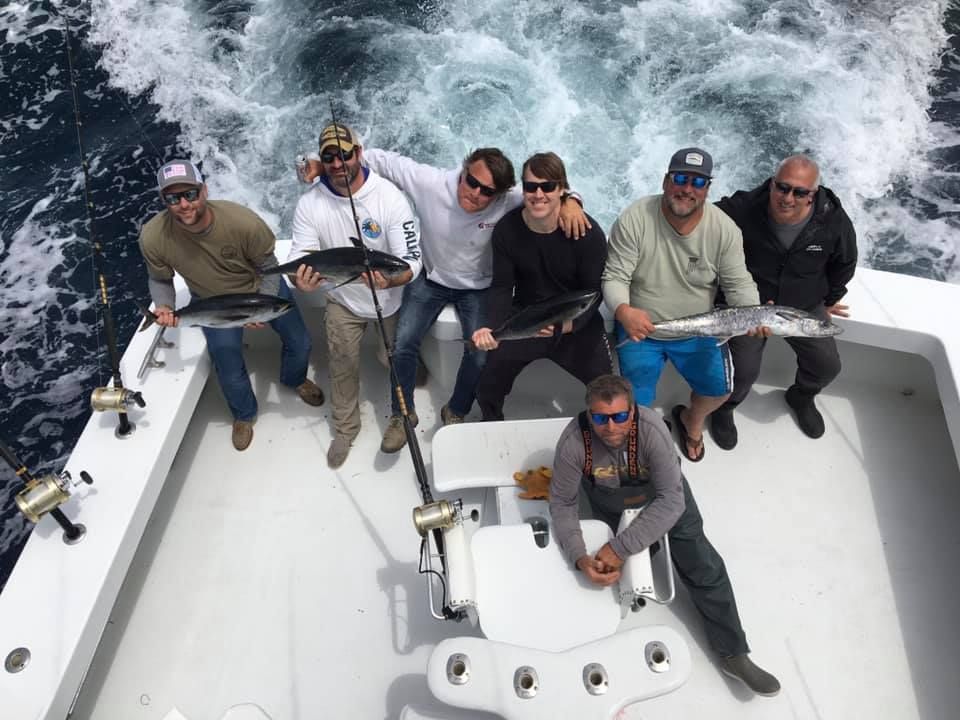Group of people on a boat, holding fish they caught; ocean backdrop.