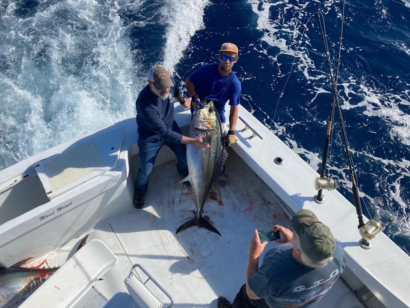Men on a boat pose with a large fish they caught, blue water surrounding them.
