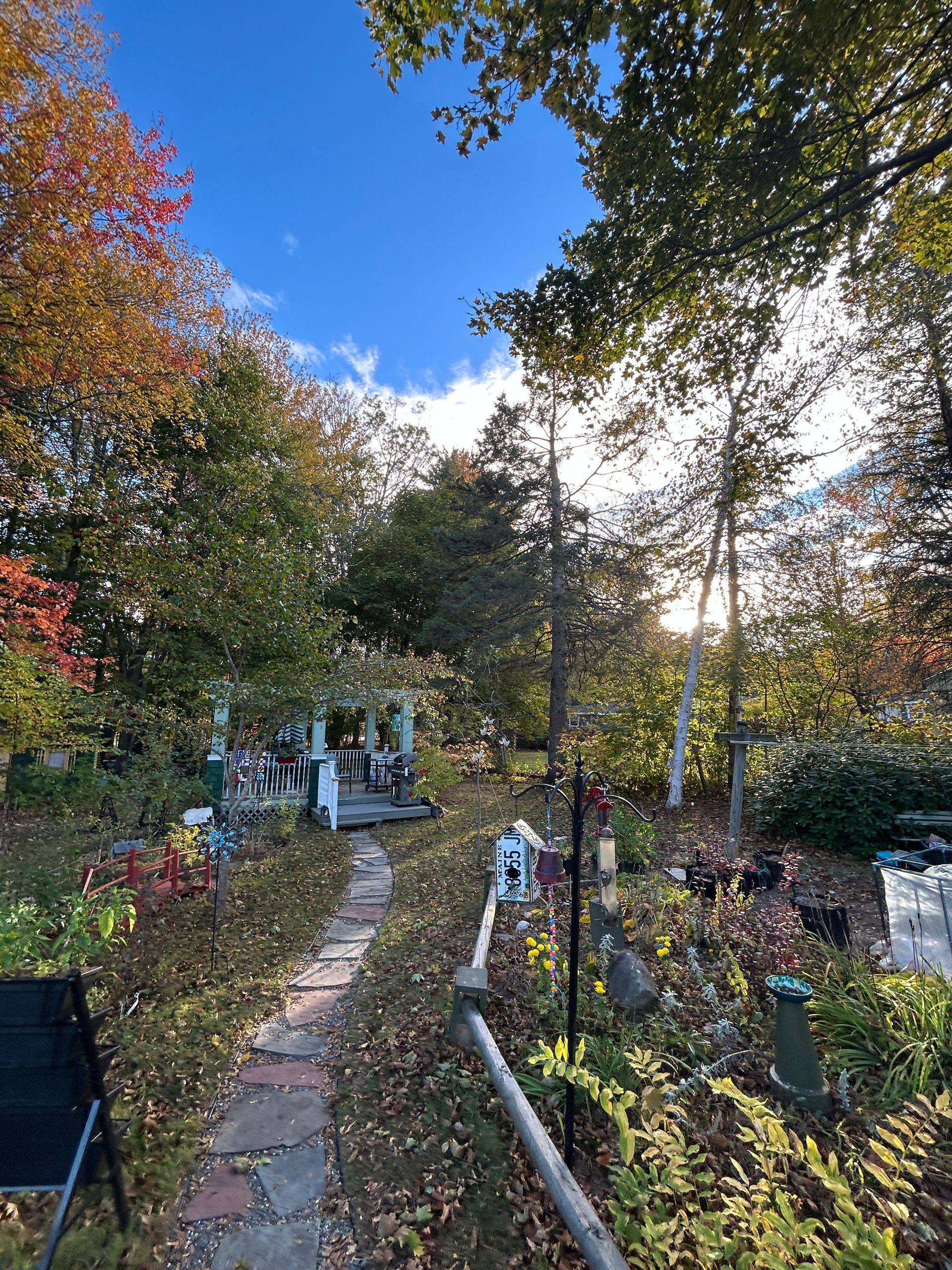 Garden path beside colorful autumn trees and a small white gate under a bright blue sky