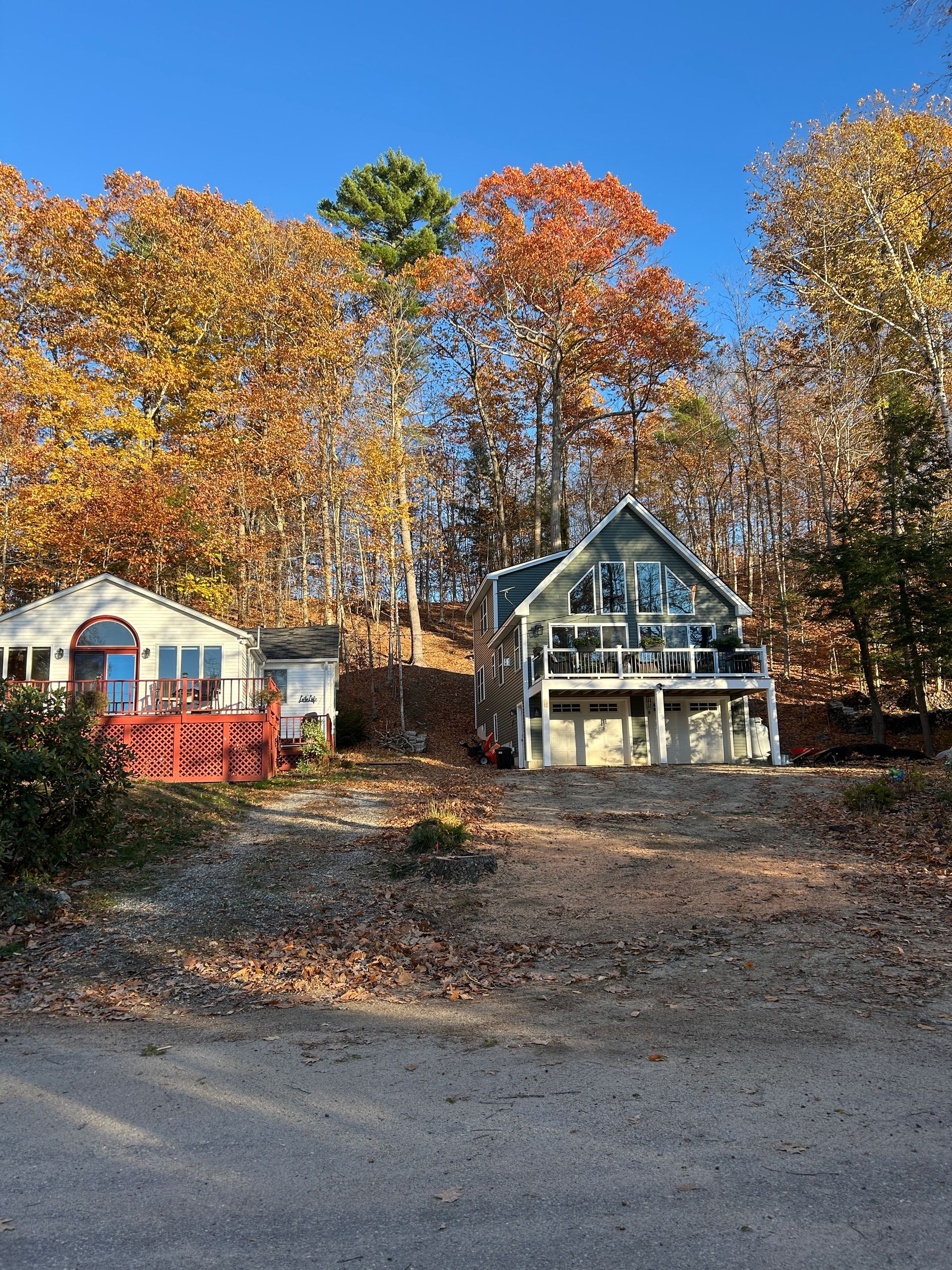 Two houses by a gravel road with autumn trees and clear blue sky