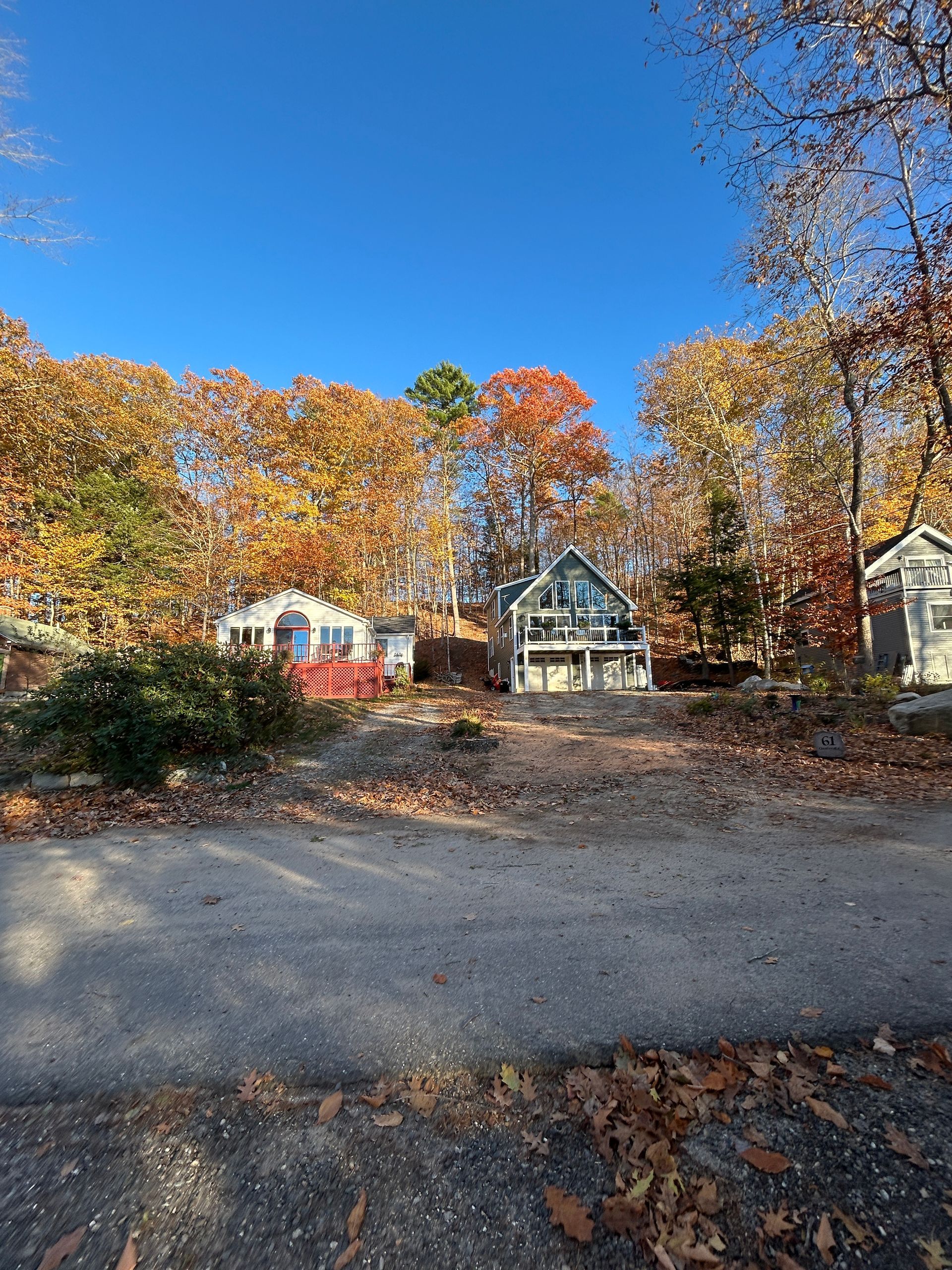 Autumn roadside scene with colorful trees and a small house under a clear blue sky